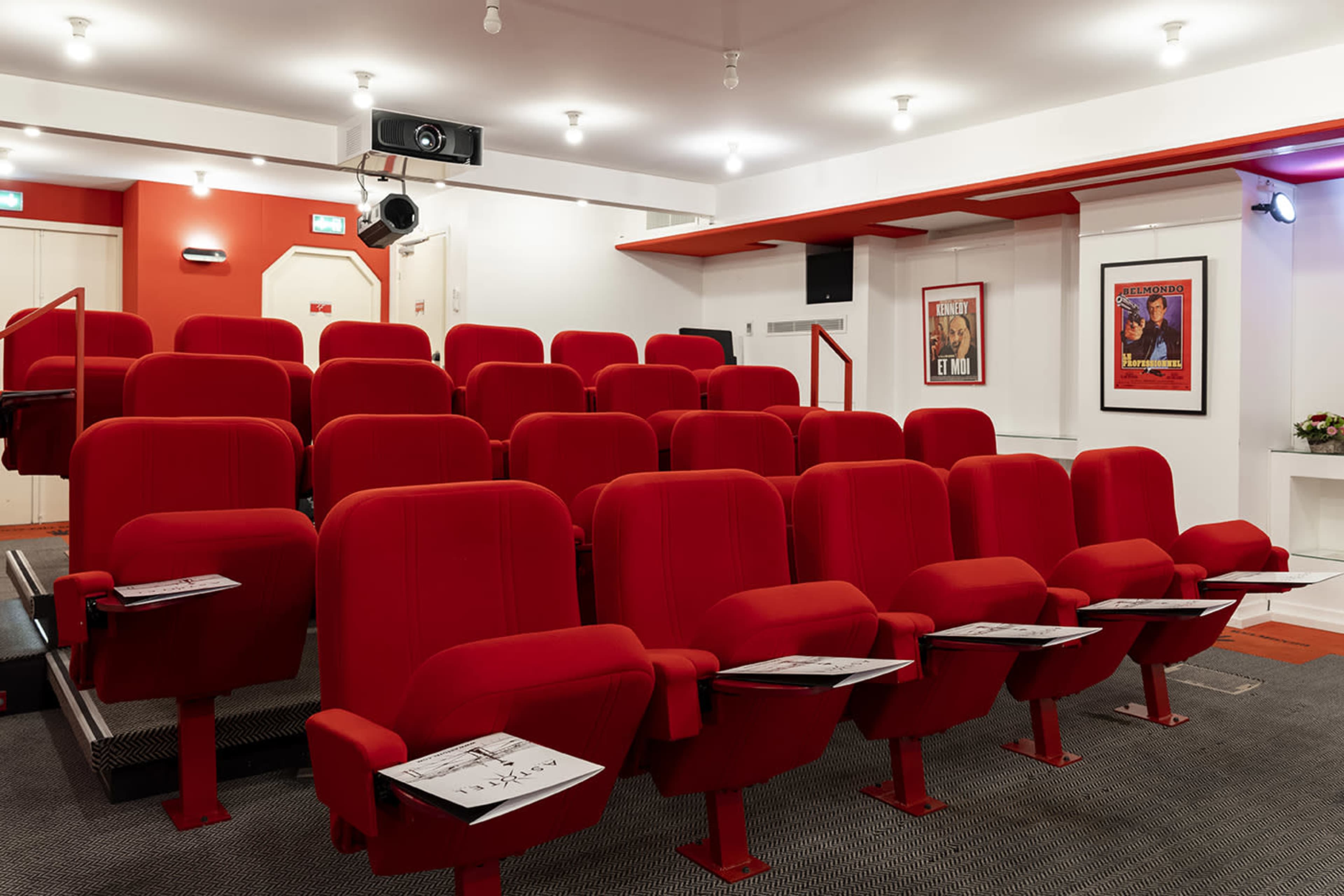 A small red theater with empty rows of plush seats and posters on the walls.