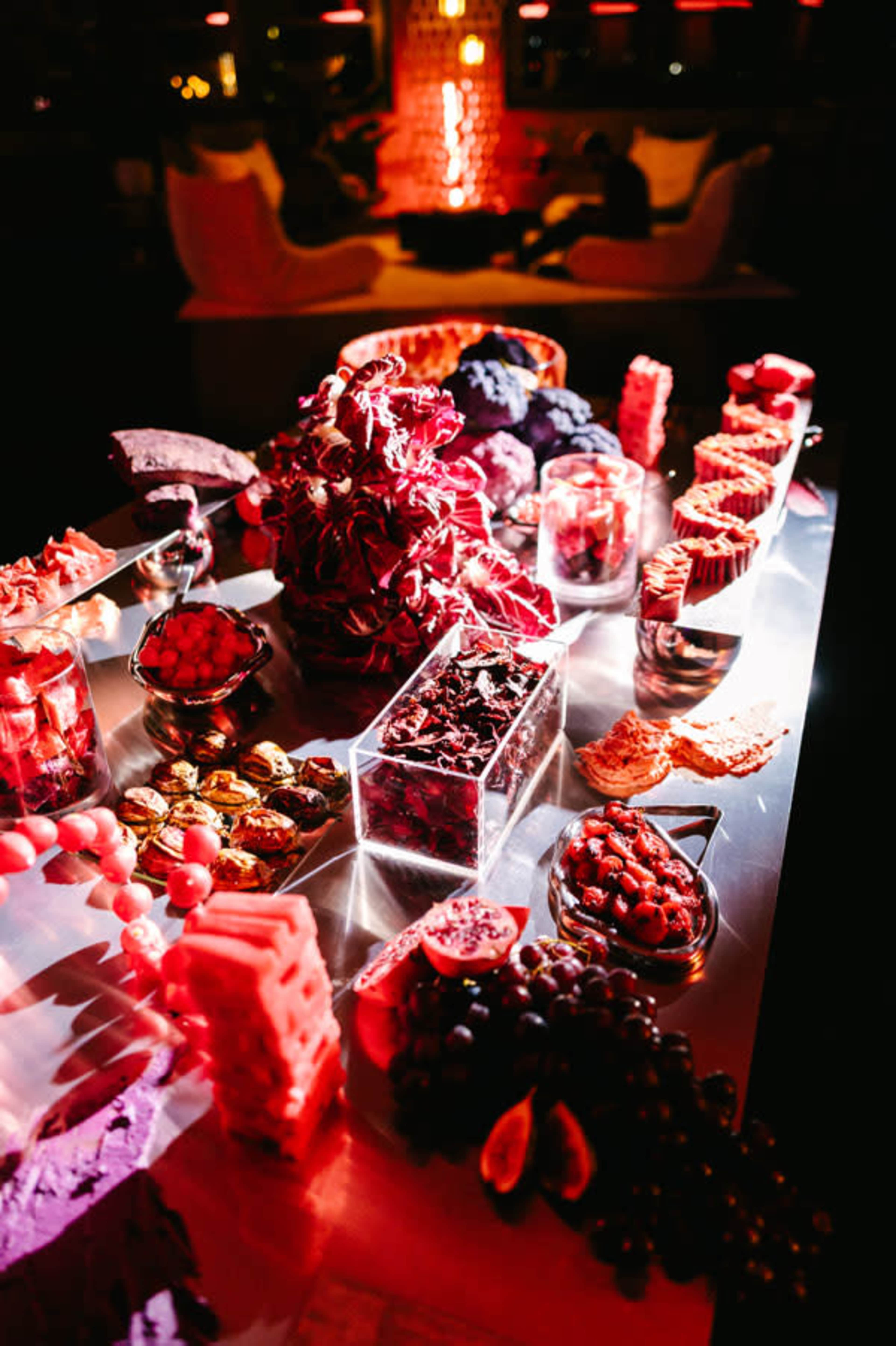 A lavish dessert table displays a variety of colorful sweets, including fruits, chocolates, and pastries, set against a dimly lit background.