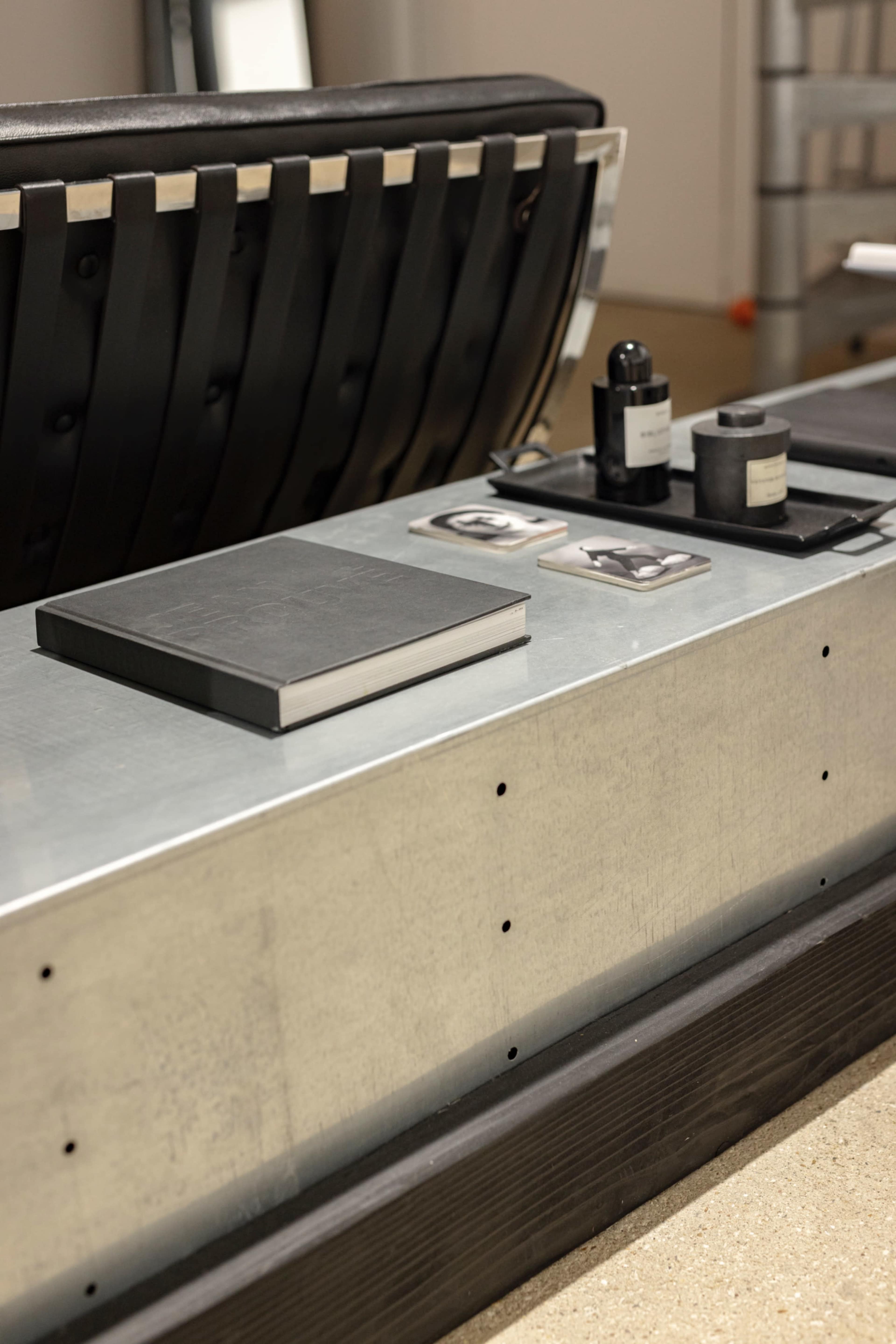 The image shows a modern, minimalist coffee table with a black book, several small objects, and framed photographs arranged on a metallic surface.