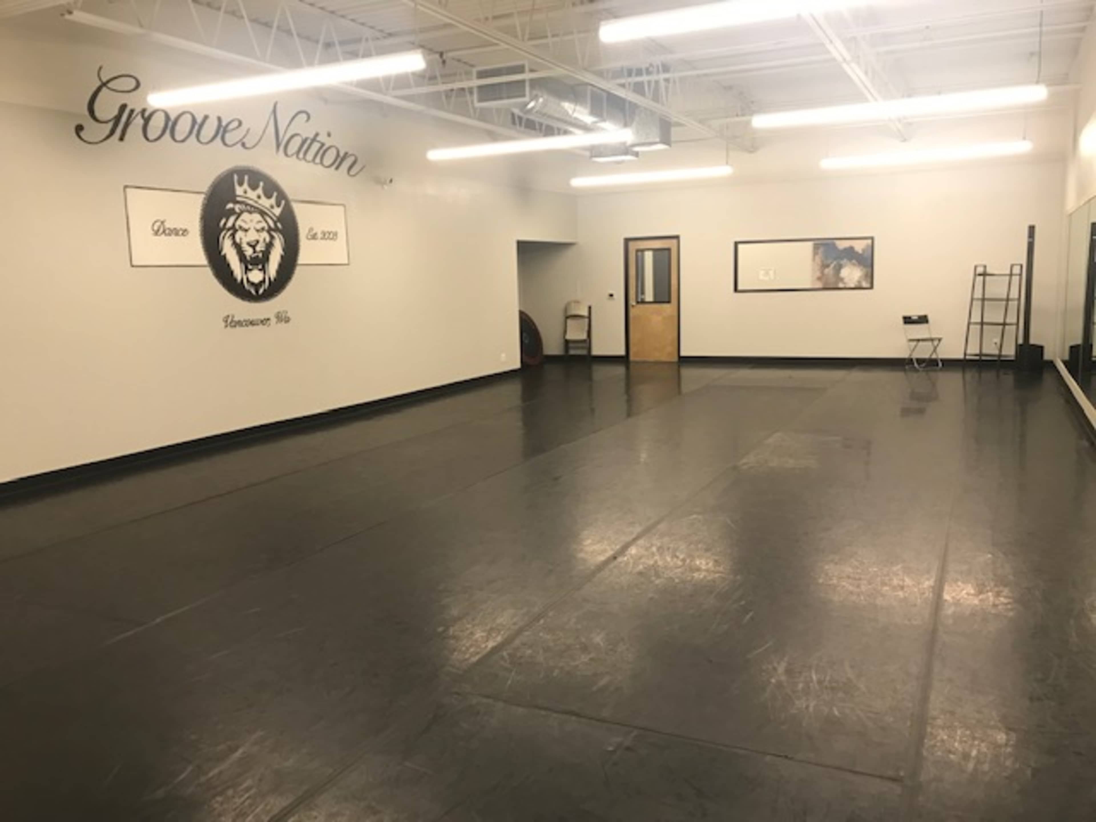 An empty dance studio with a black floor and mirrored walls, featuring the name "Groove Nation" on one wall.