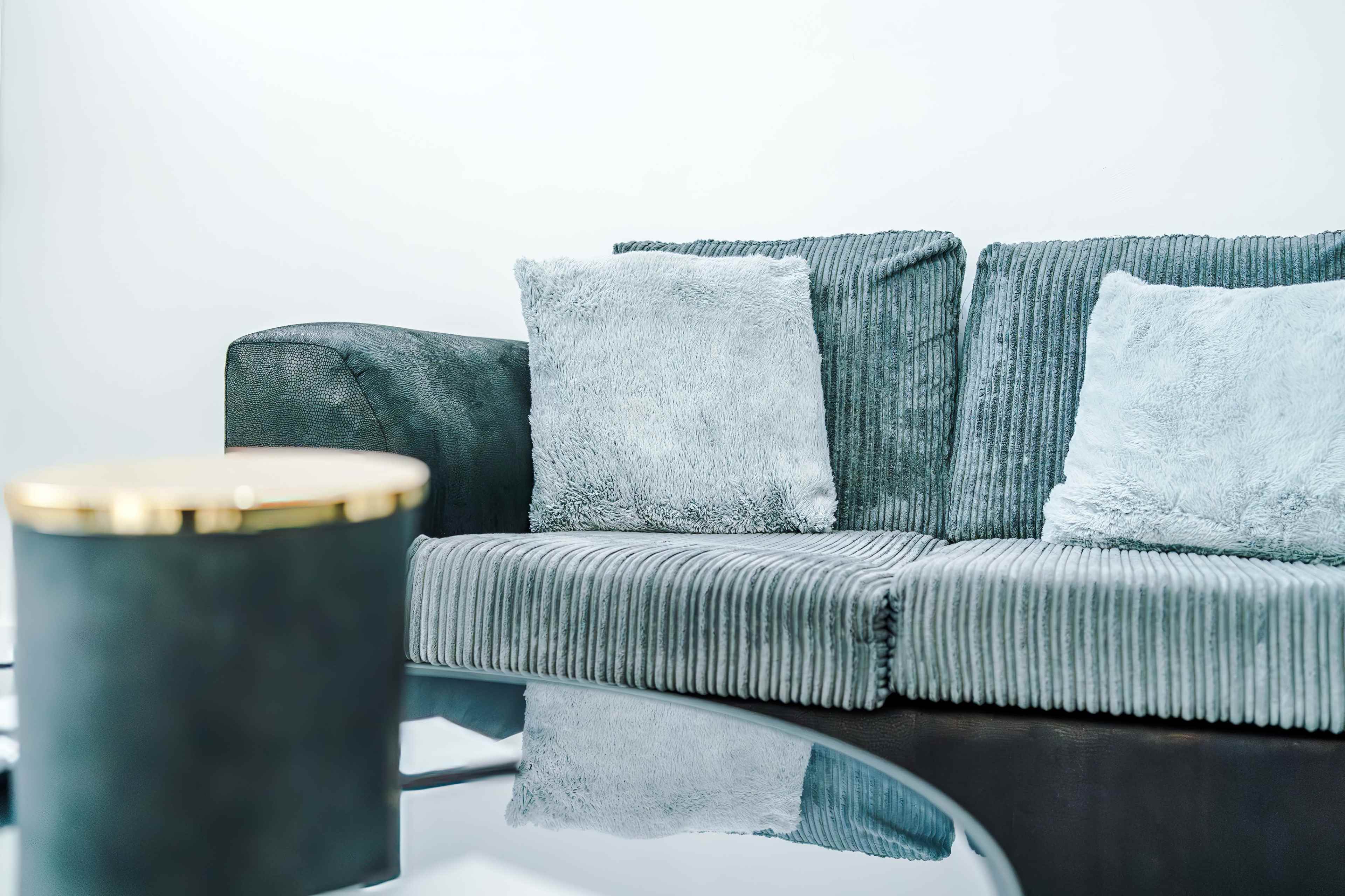 A grey-striped couch with two light blue pillows sits next to a glass coffee table.