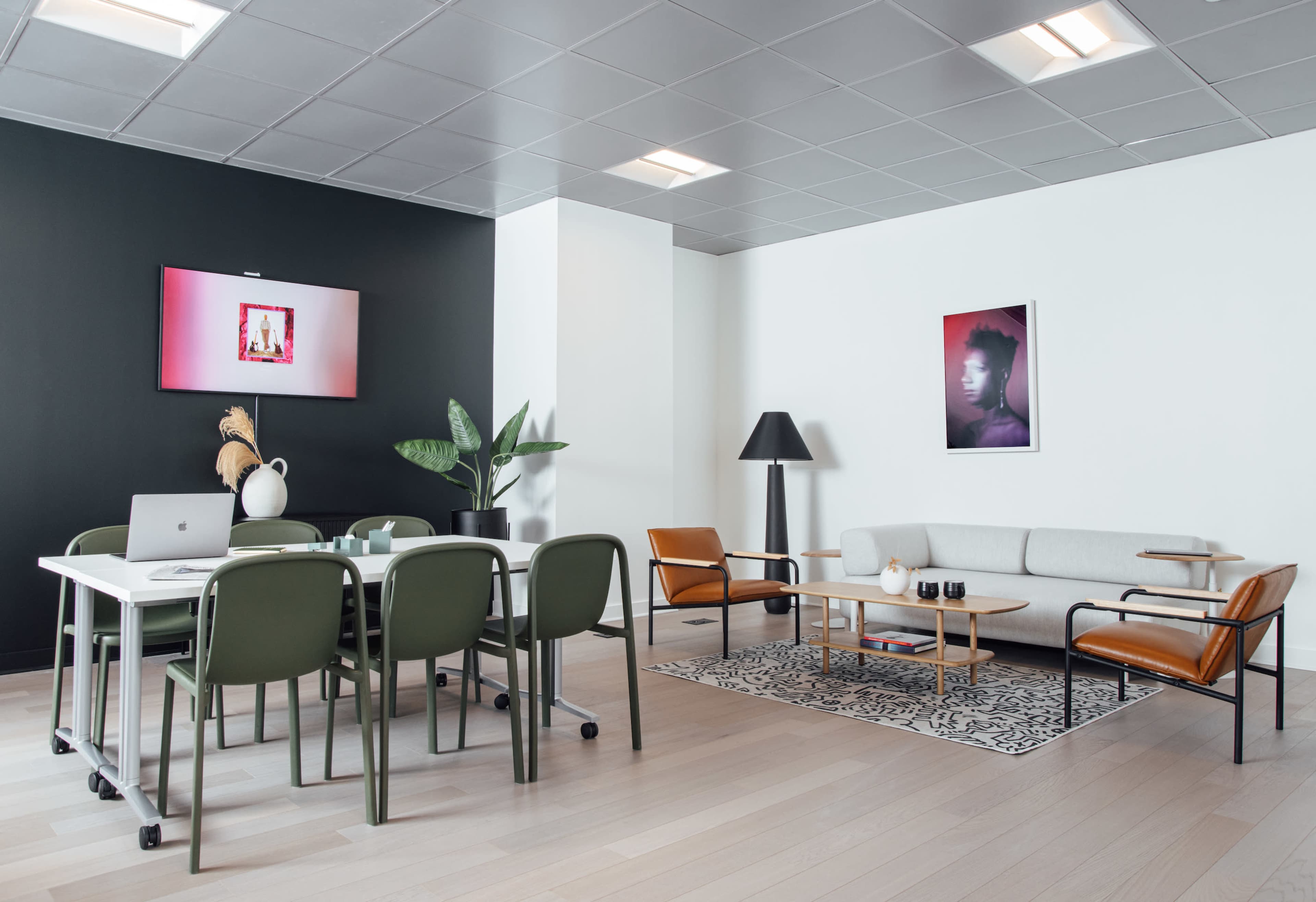 A modern office space with a dining table and chairs, a sofa, a plant, and framed art on the walls.