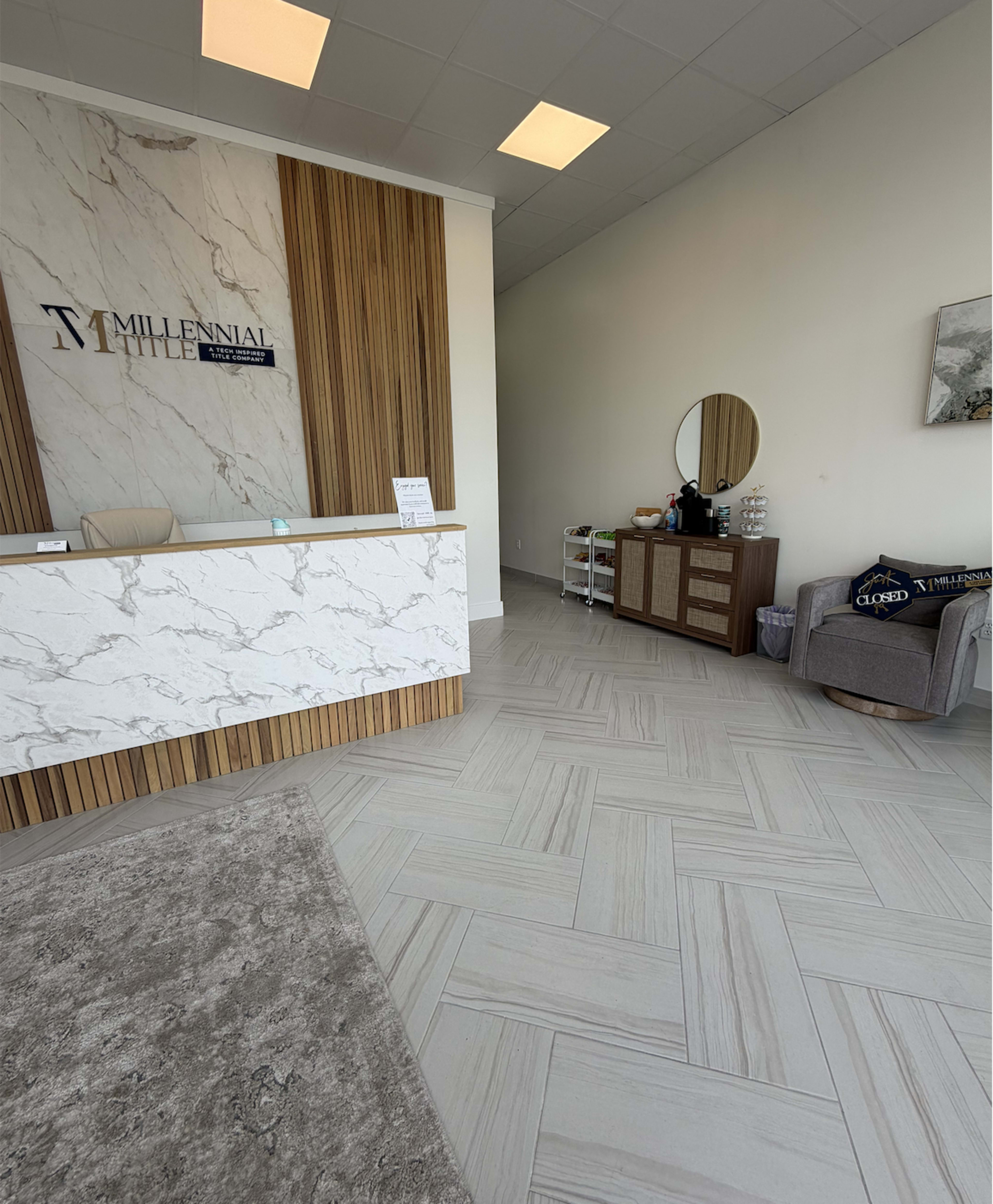 The image shows a modern reception area featuring a marble front desk, wooden paneling, a round mirror, and a set of cabinets against the wall.