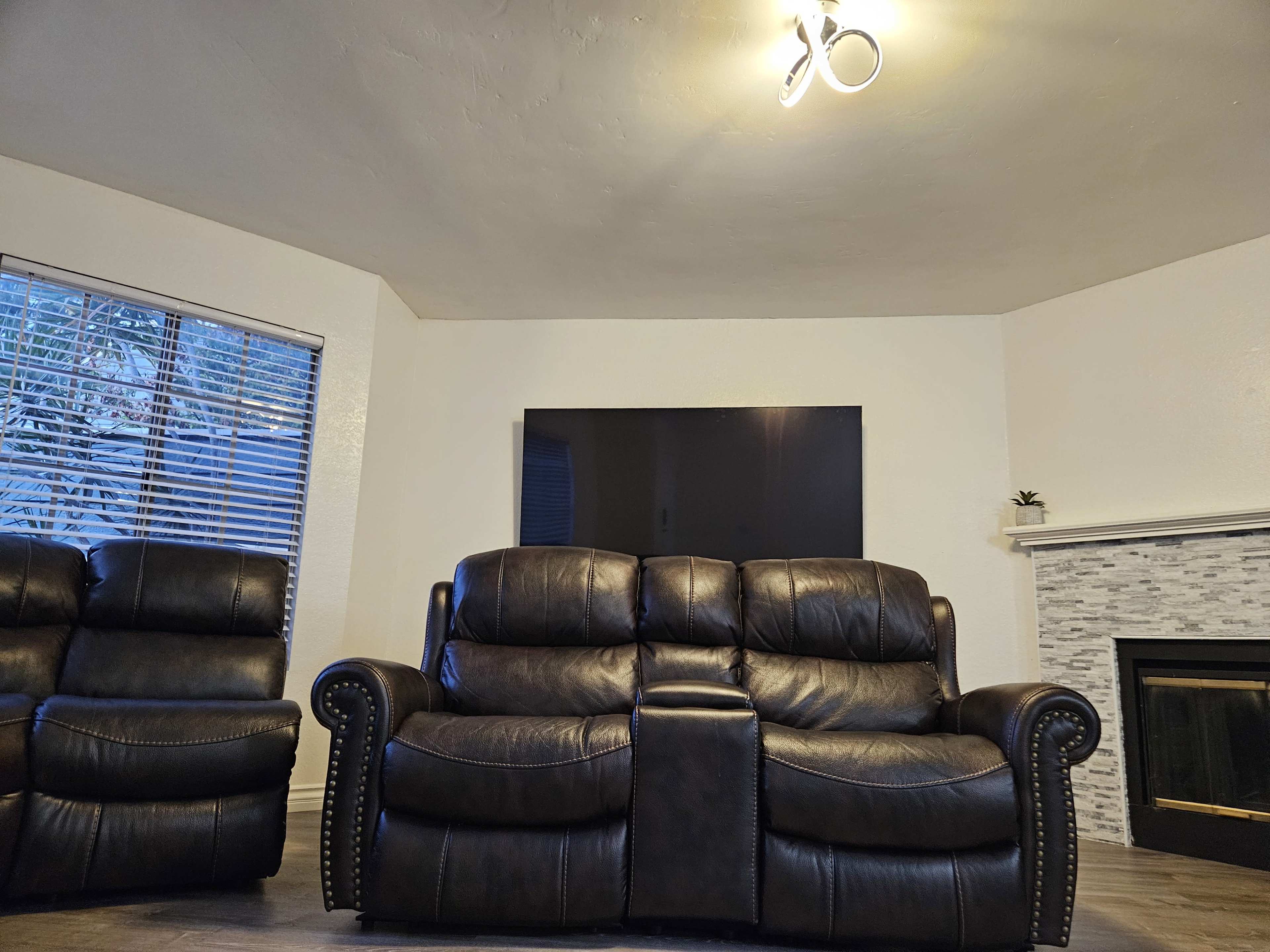 A spacious living room features a dark leather couch facing a wall-mounted television above a stone fireplace.
