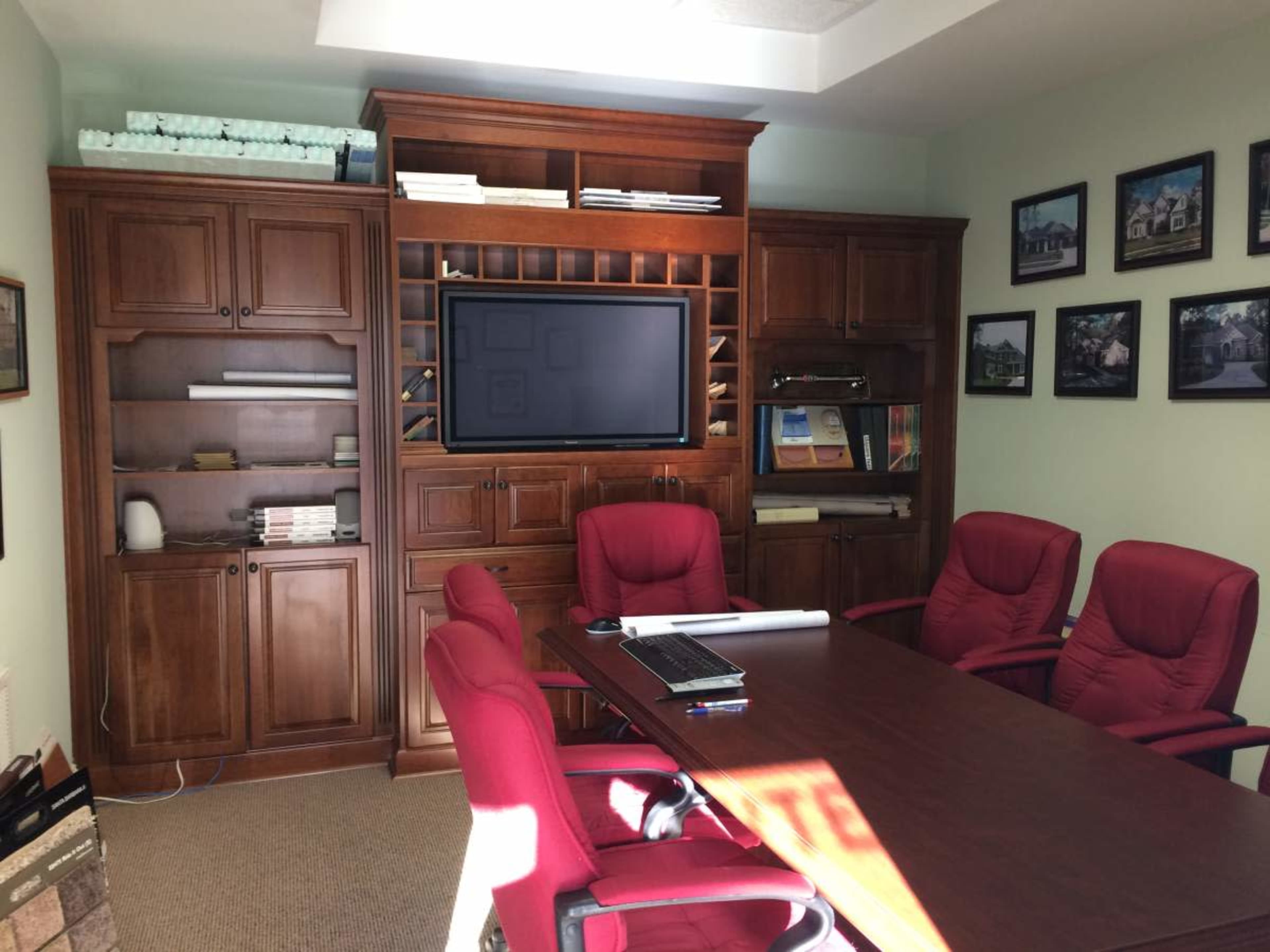 A conference room with a wooden table, red chairs, and a wall-mounted television, surrounded by shelves holding books and documents.