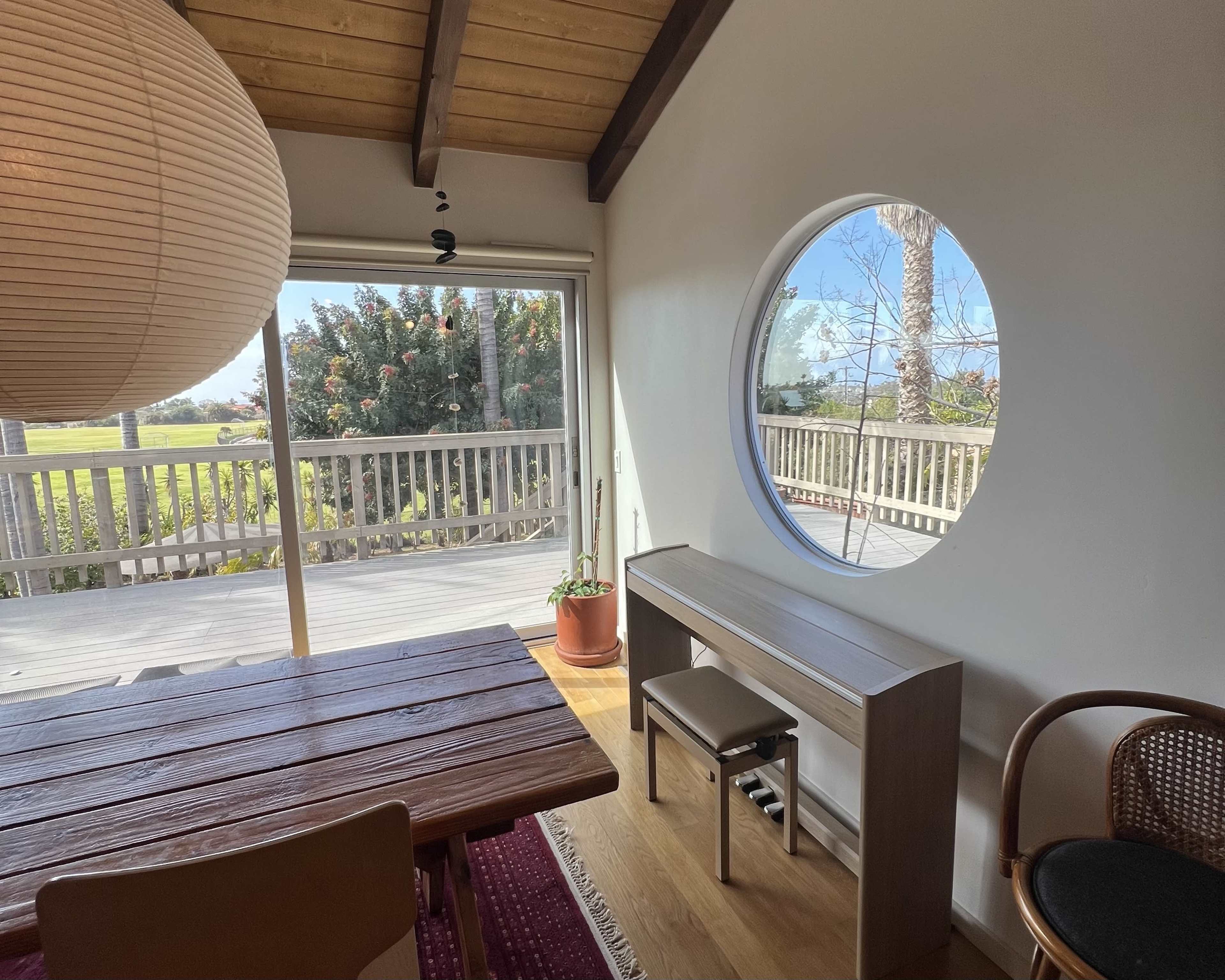 A round window frames a view of greenery outside, with a wooden dining table and a minimalist sideboard in the interior space.