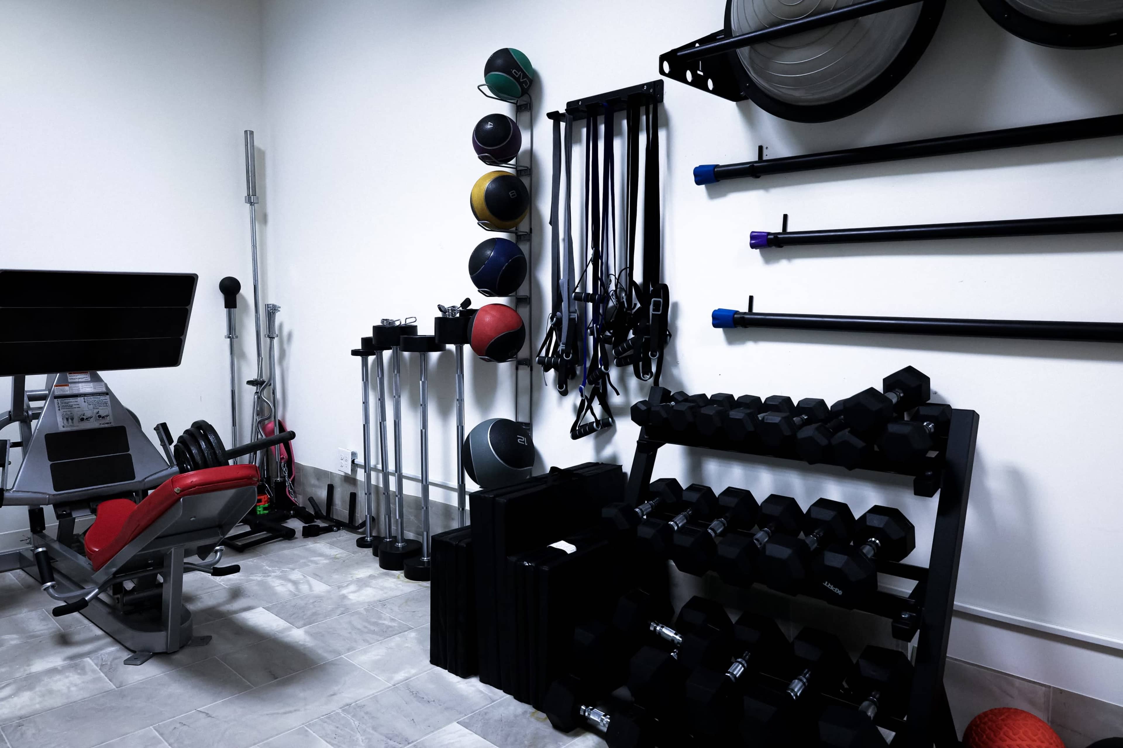 A home gym with various weights, exercise equipment, and resistance bands neatly organized against the walls.