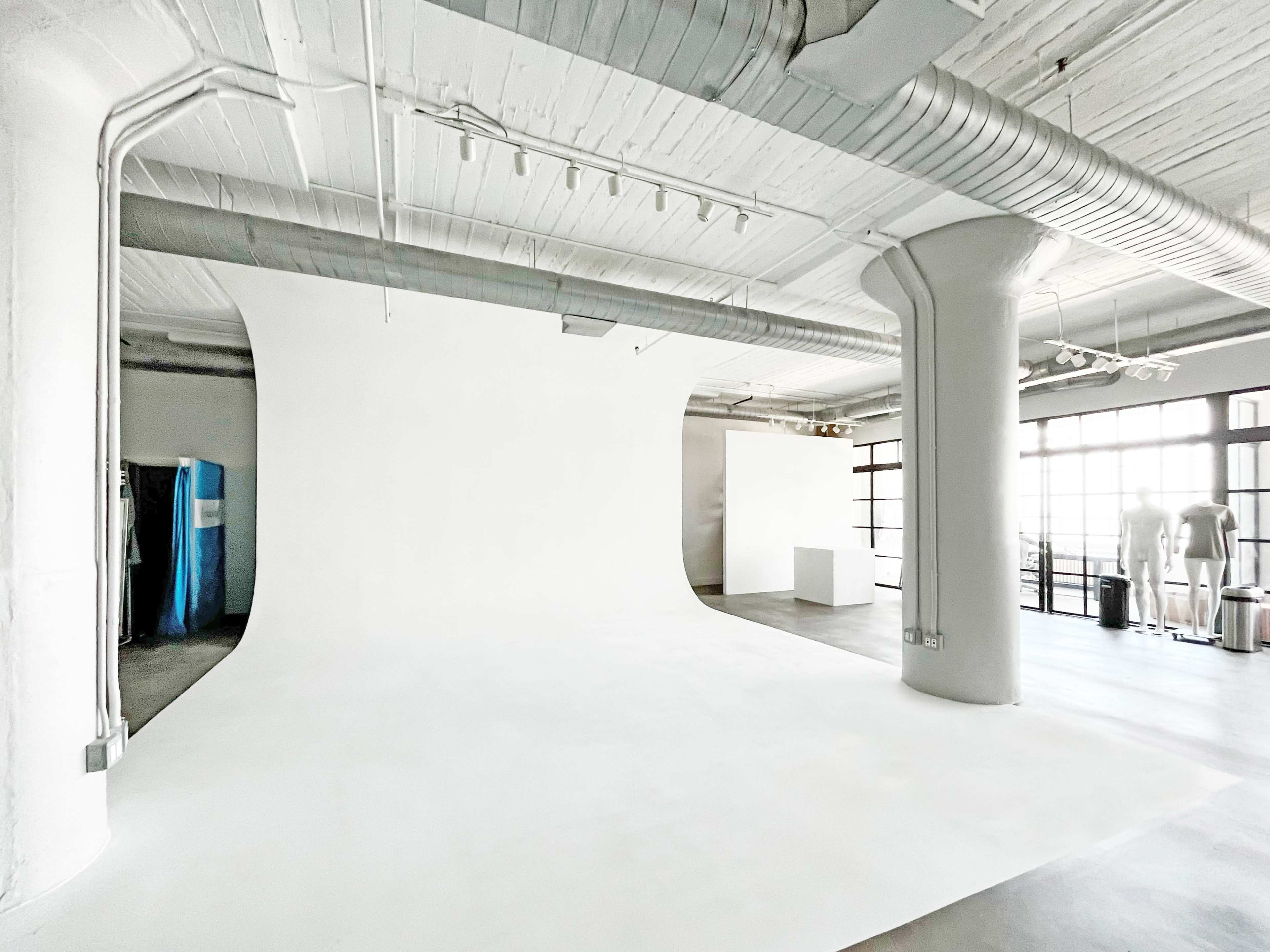 A spacious studio with a seamless white backdrop, large windows, and various equipment arranged around the room.