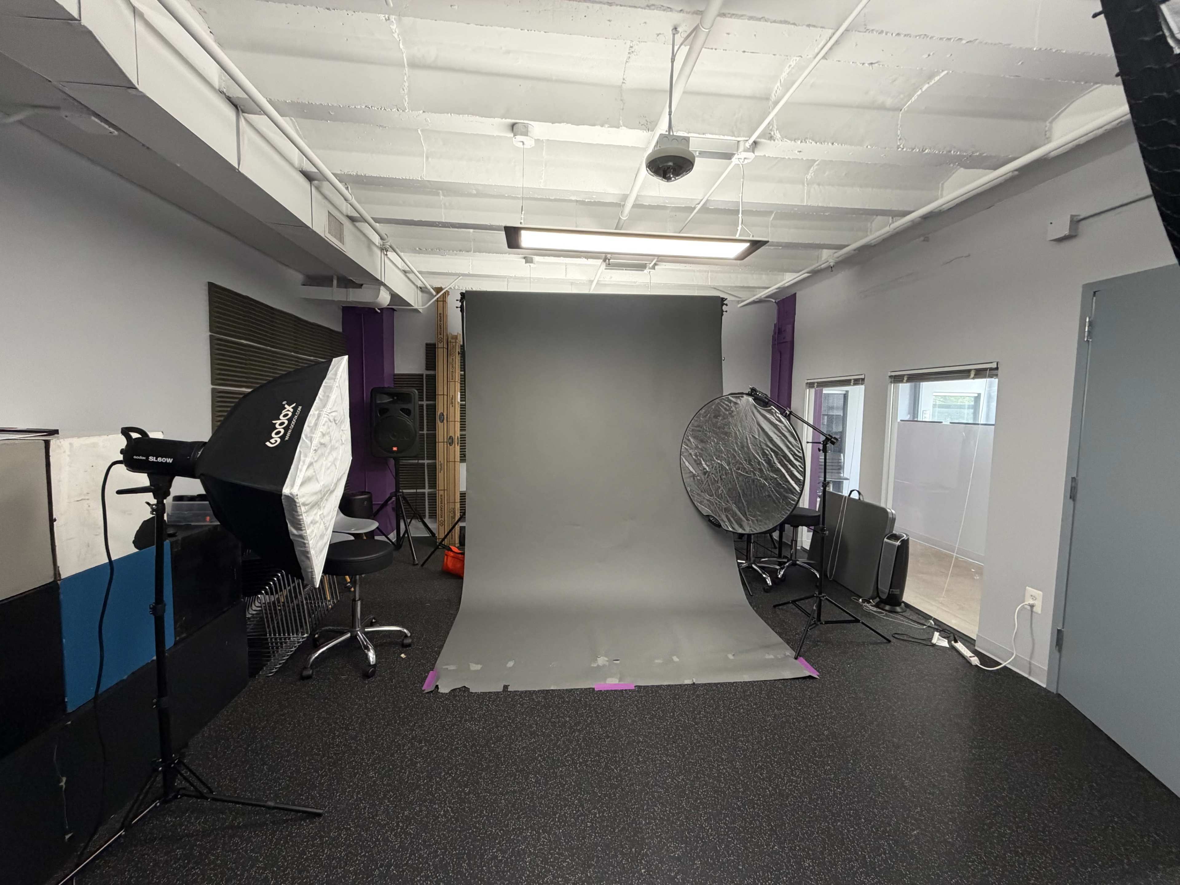 The image shows a photography studio setup with a gray backdrop, lighting equipment, and various props arranged in the space.