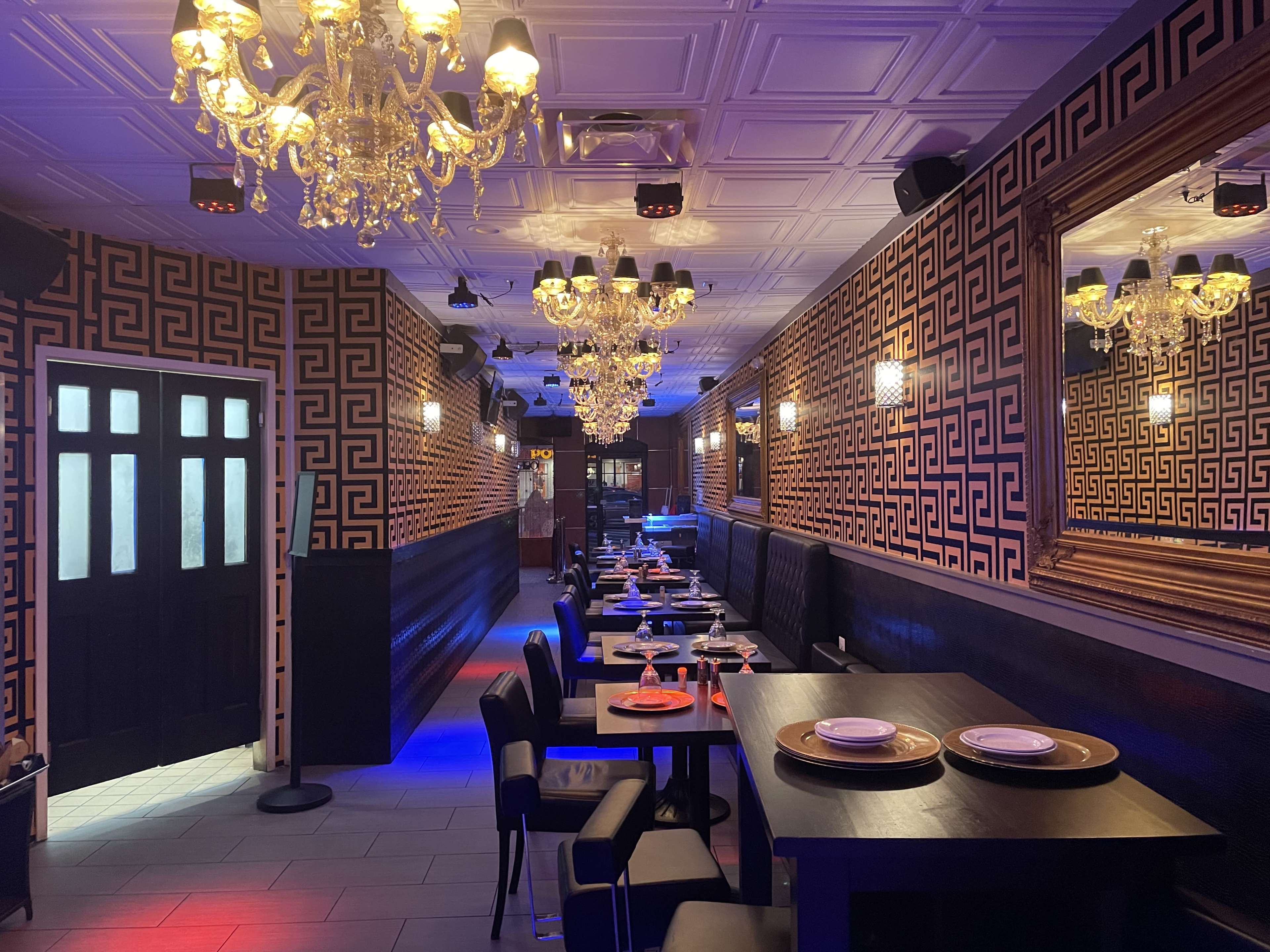 A restaurant interior with patterned walls, chandeliers, and tables set for dining.