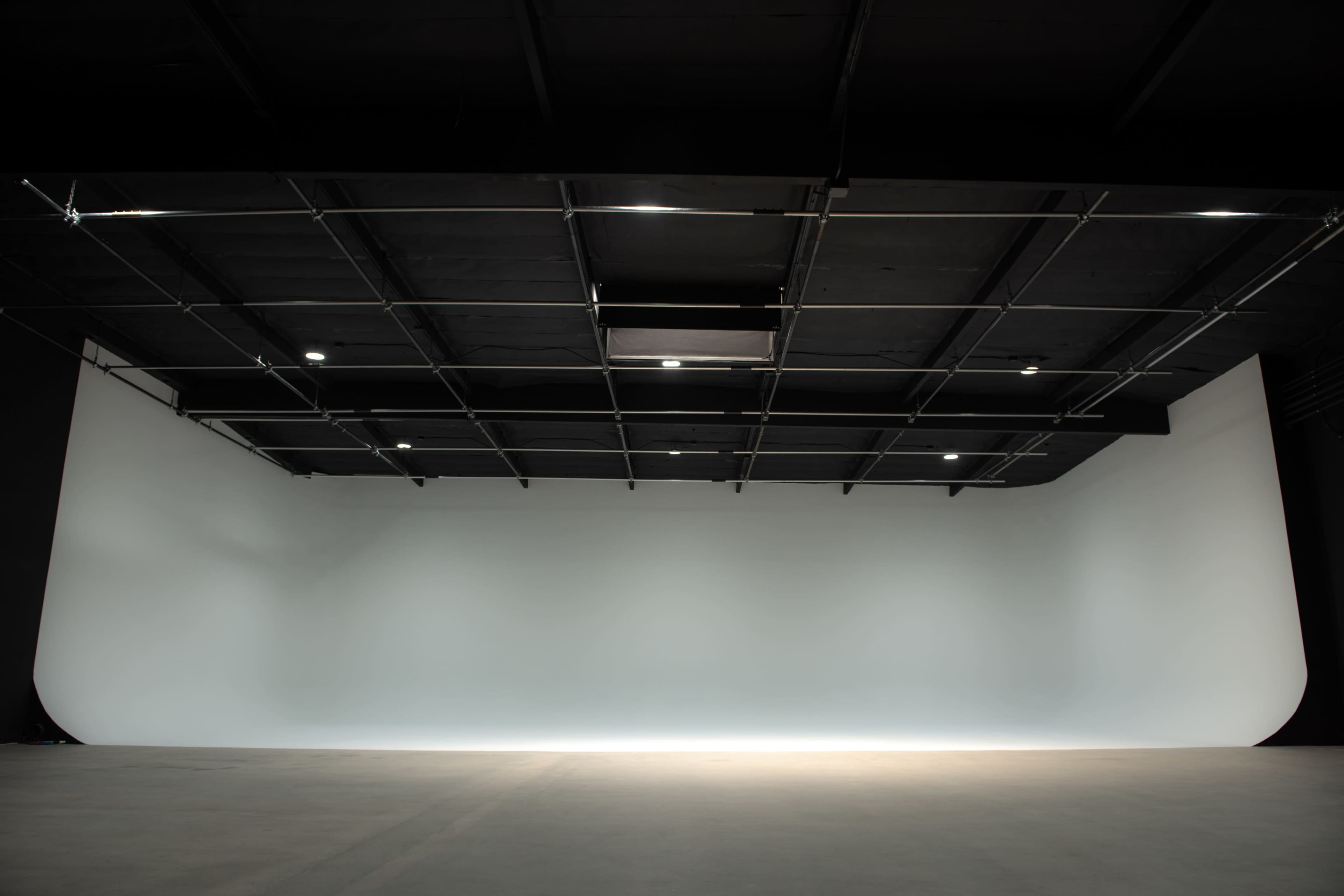 A large, empty studio space with a seamless white backdrop and overhead lighting.