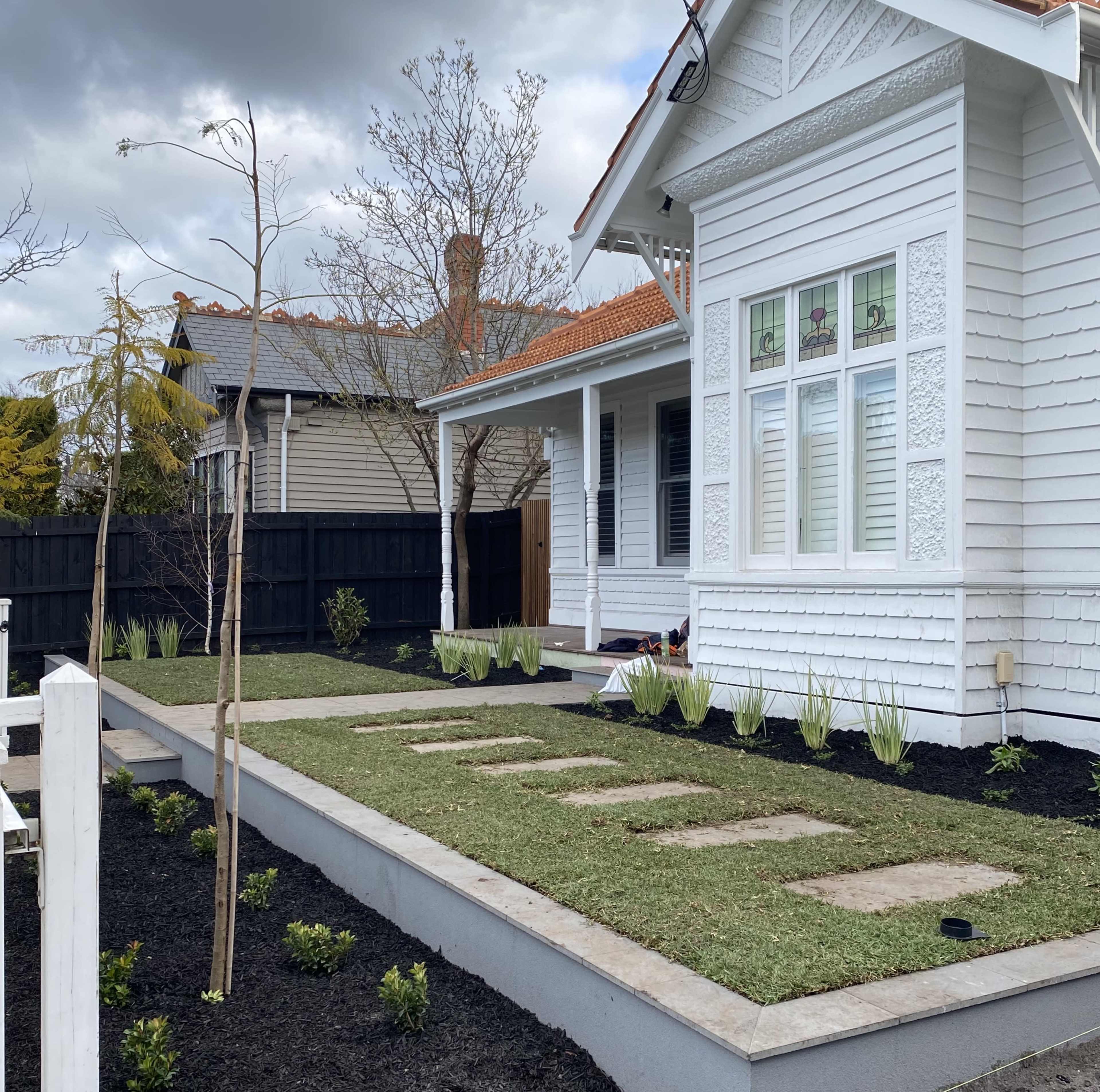 A landscaped front yard with a house featuring white siding, a stone path, and newly planted greenery surrounded by dark mulch.