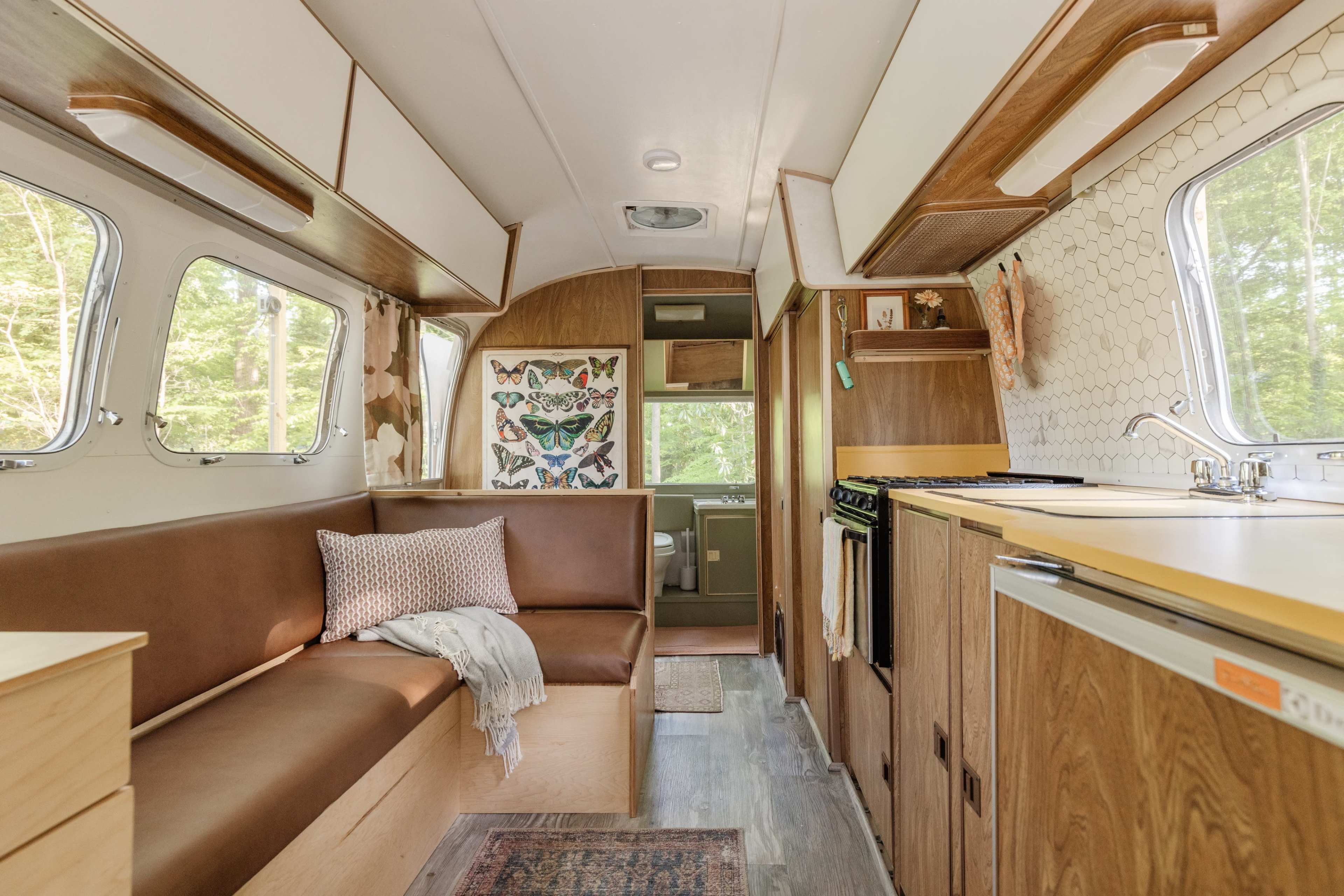 The image shows the interior of a camper van featuring a seating area, kitchen, and decorated walls with a butterfly print.