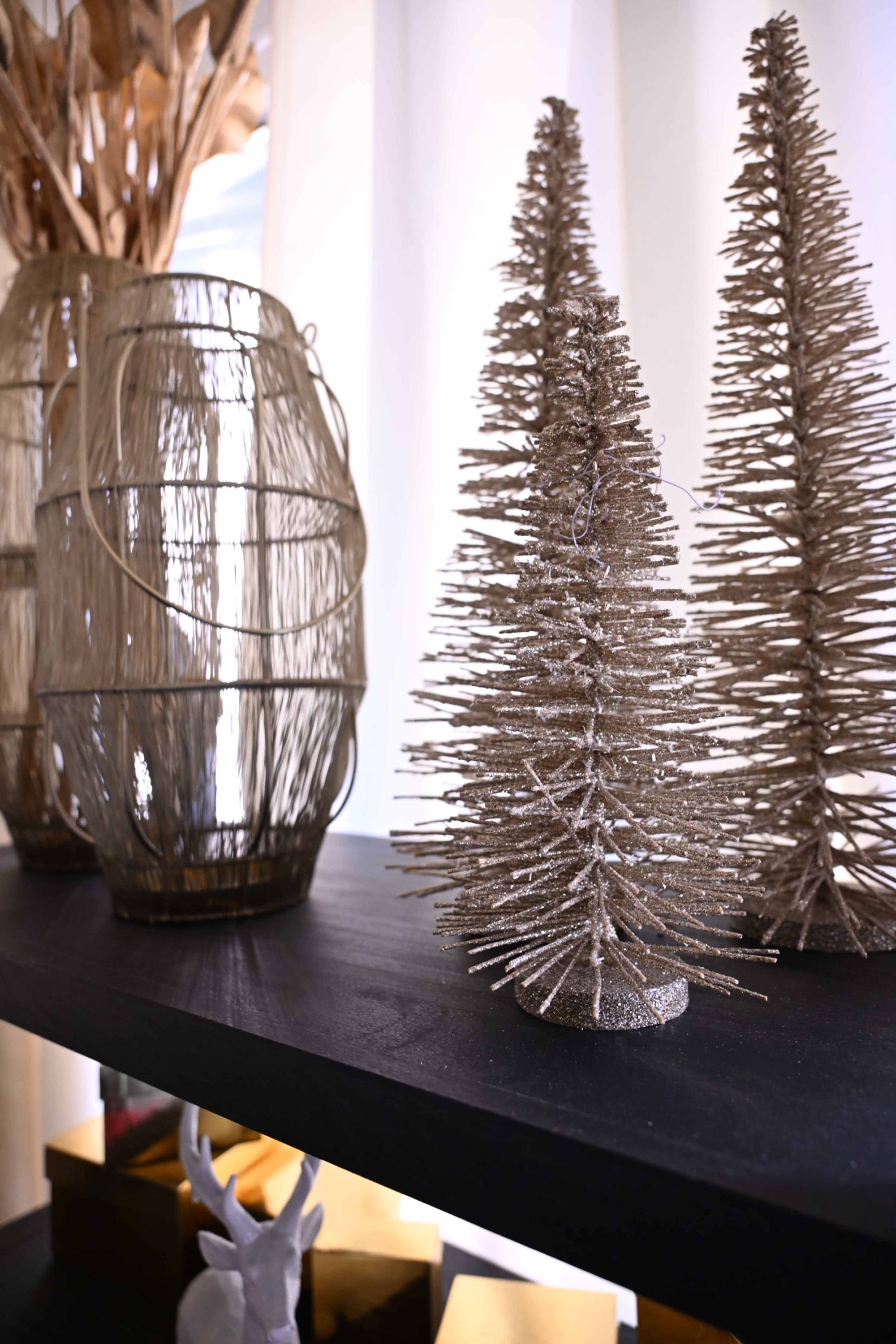 A black shelf displays three decorative gold-colored trees alongside a woven vase with tall decorative branches.