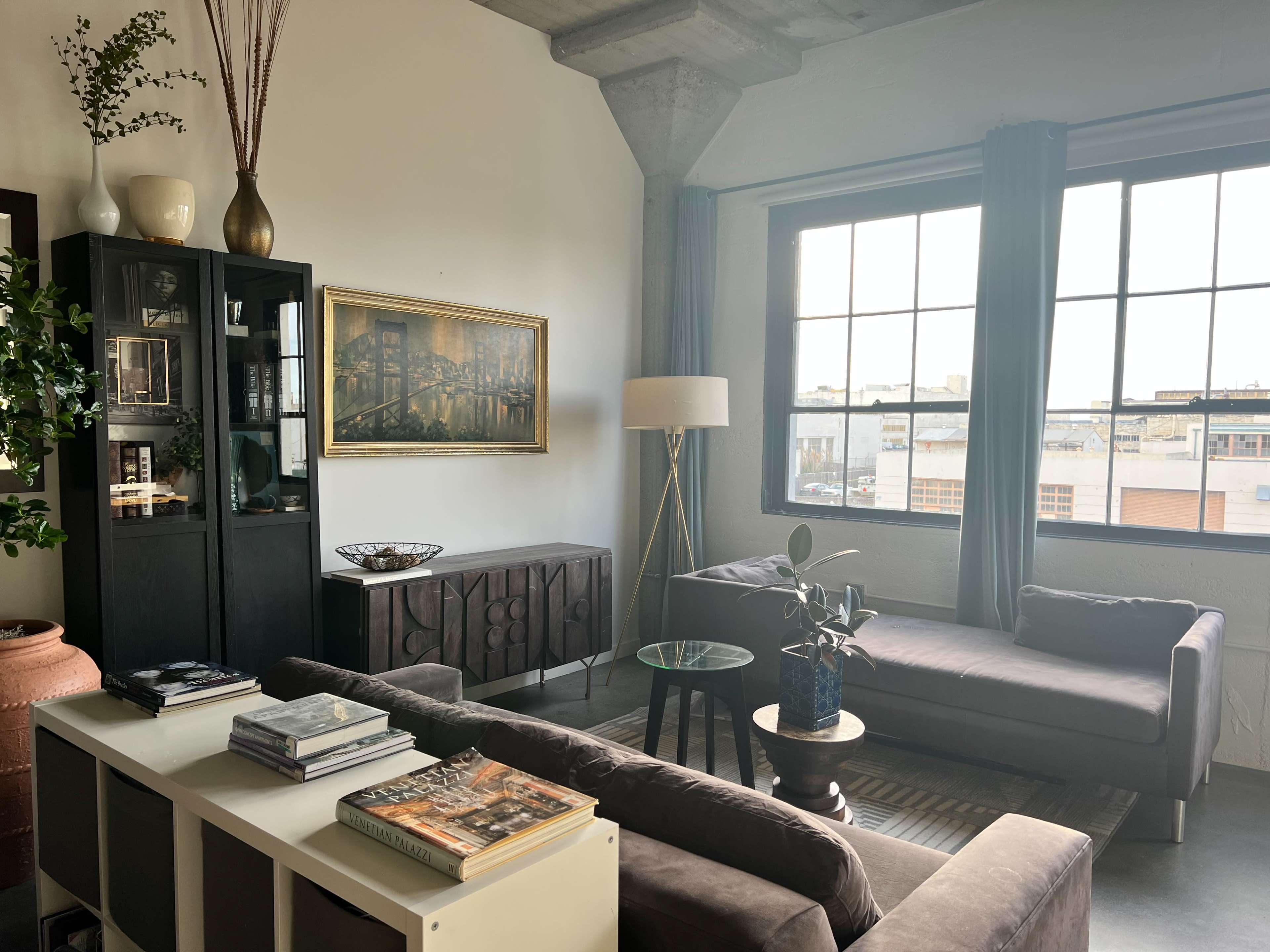 The image shows a modern living room with a gray sofa, a coffee table, a tall lamp, and large windows letting in natural light.