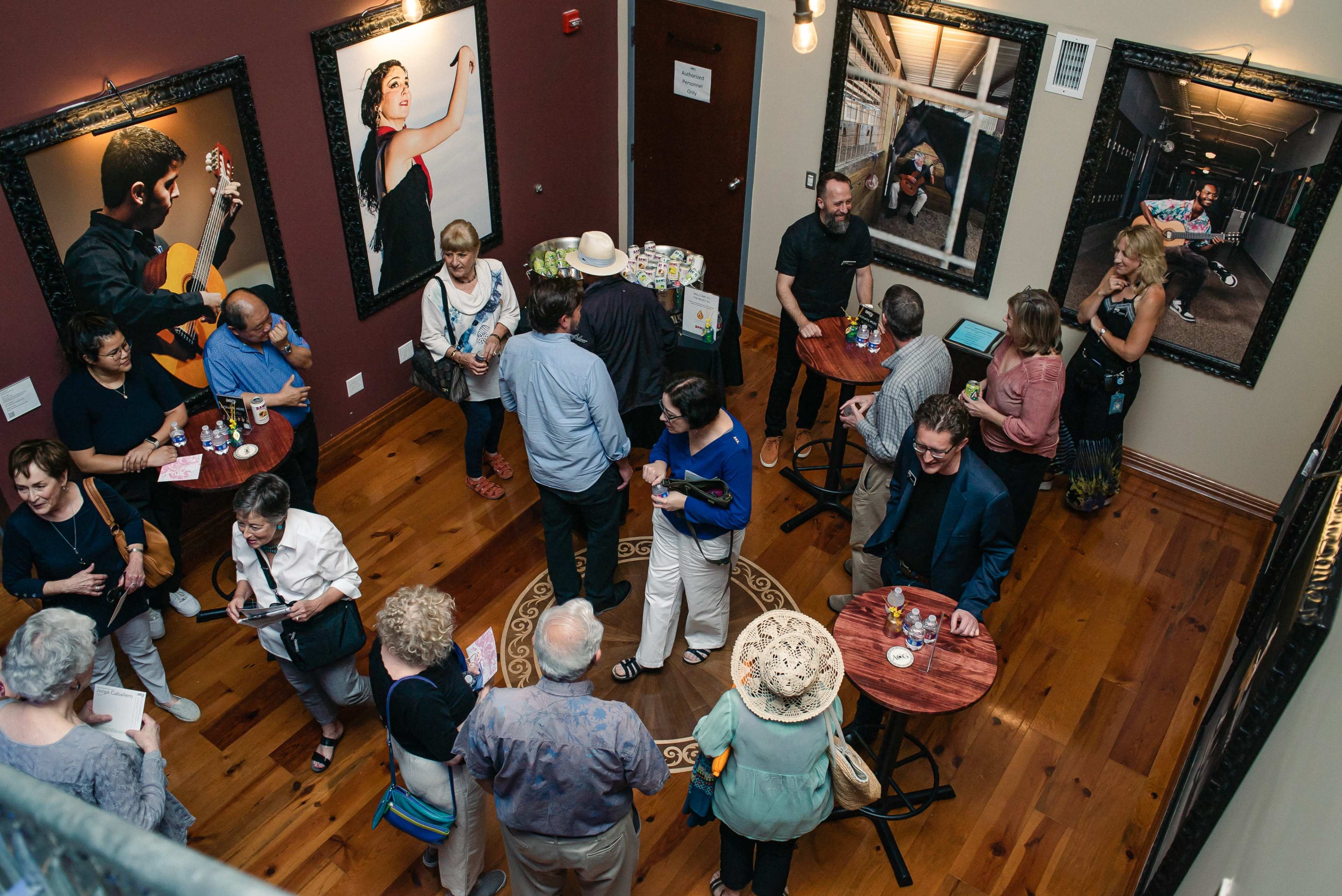 A group of people socialize around small tables in a gallery featuring large framed photographs on the walls.