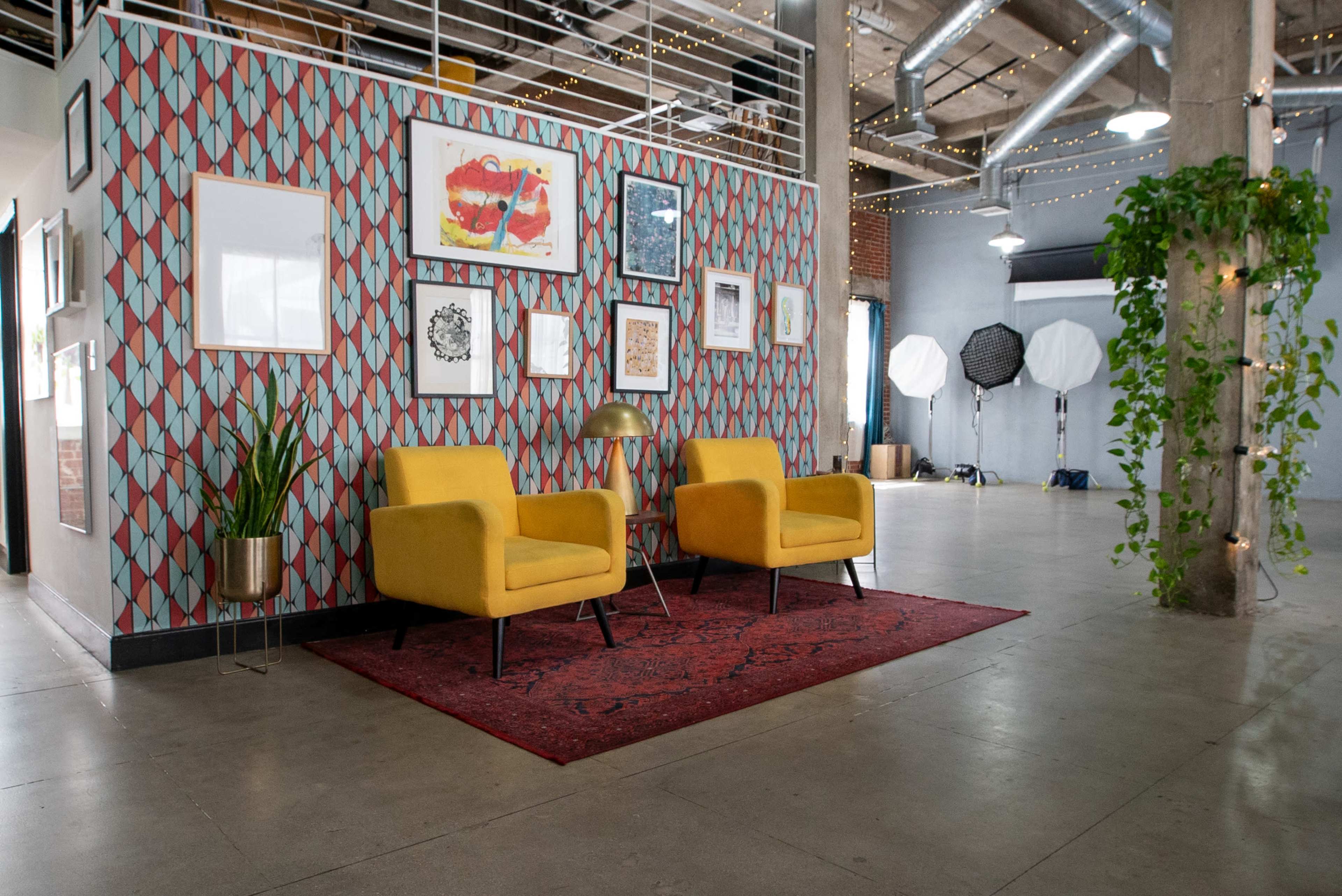 A modern open space featuring two yellow chairs on a red rug in front of a patterned wall adorned with various framed artworks.
