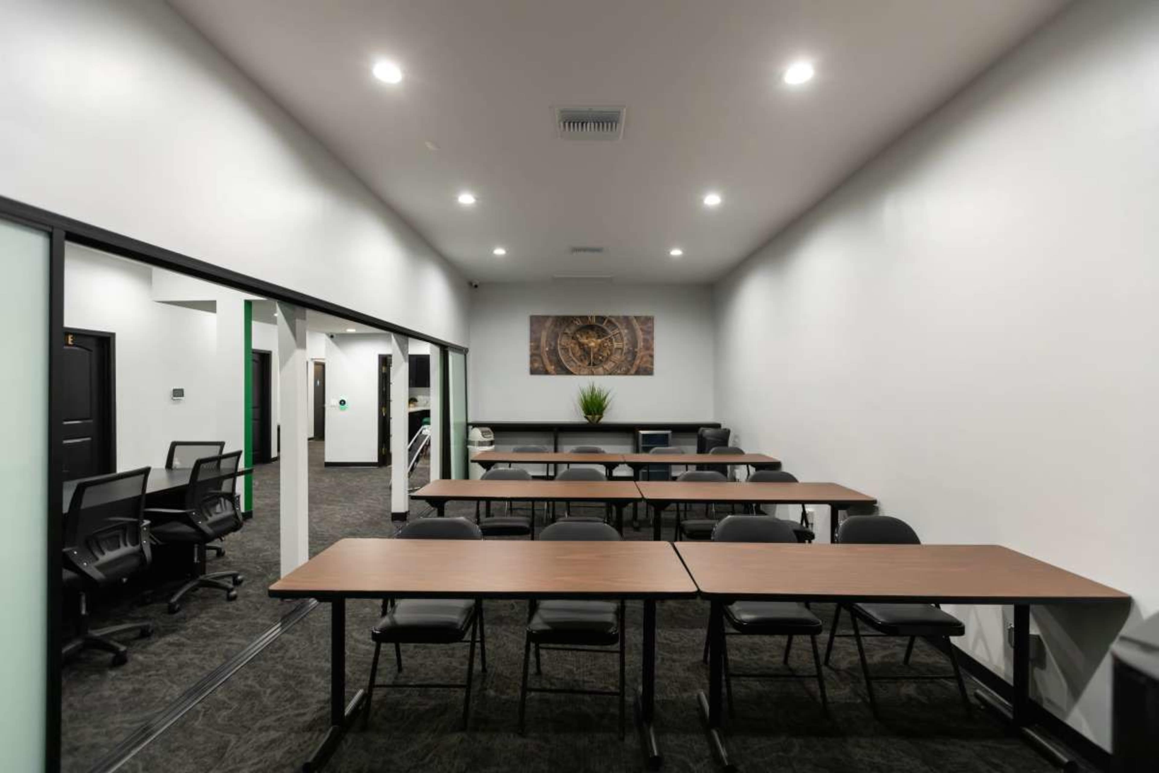 The image shows a modern, sparsely furnished conference room with several tables and chairs arranged in a row.