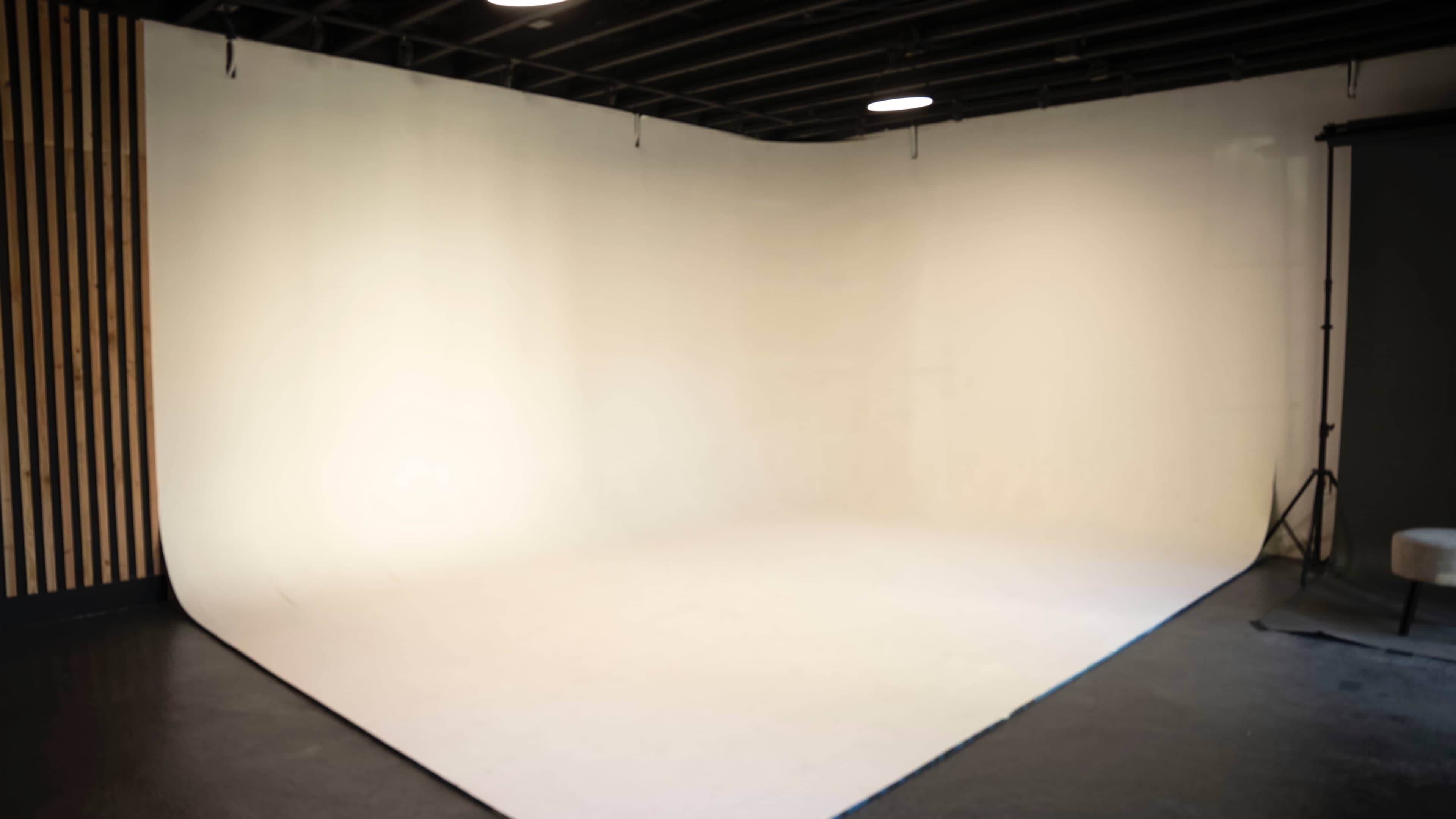 A spacious photography studio with a white backdrop and minimal furnishings.