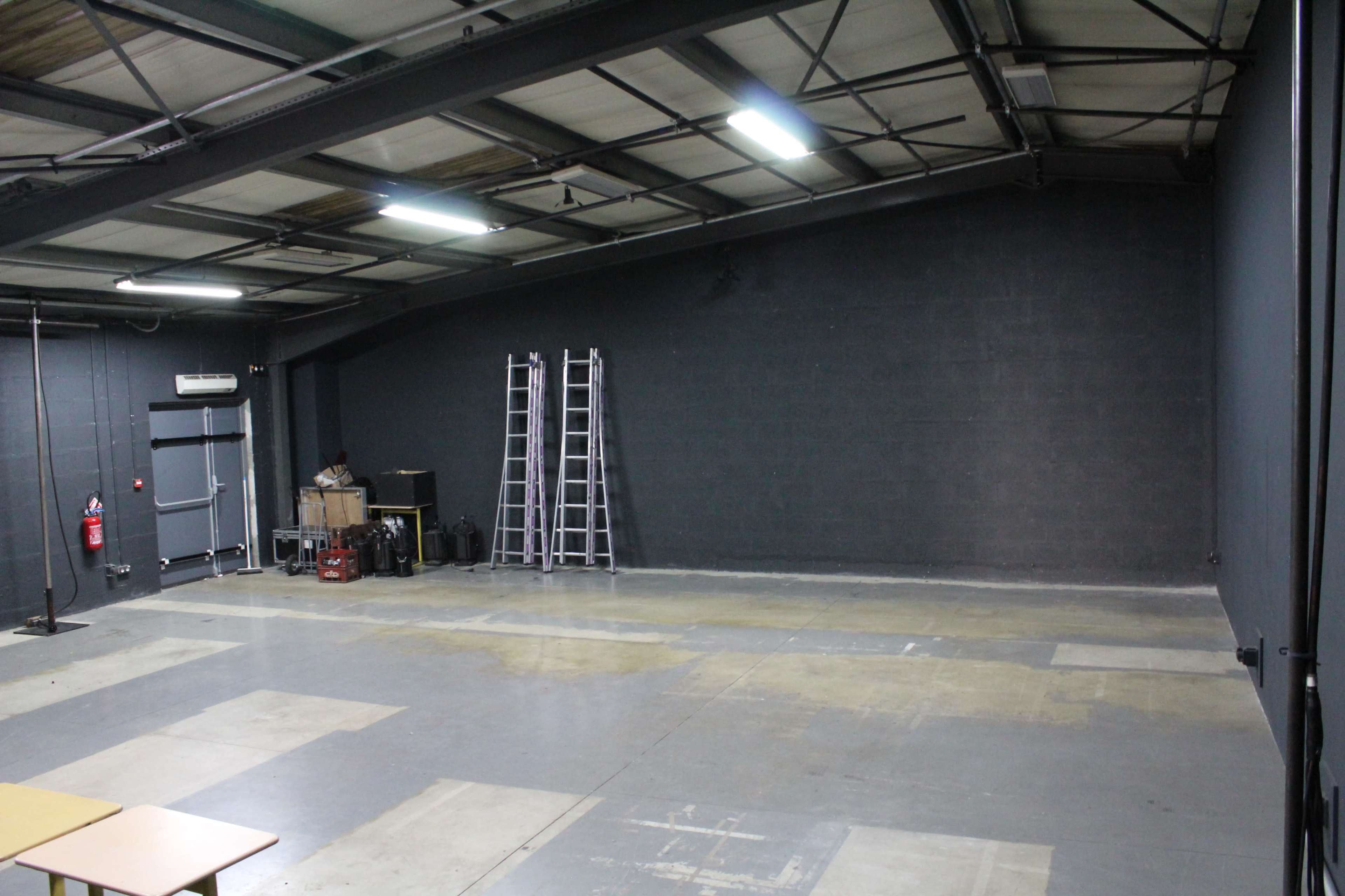 An empty warehouse space features a concrete floor, gray walls, and two ladders against the back wall.
