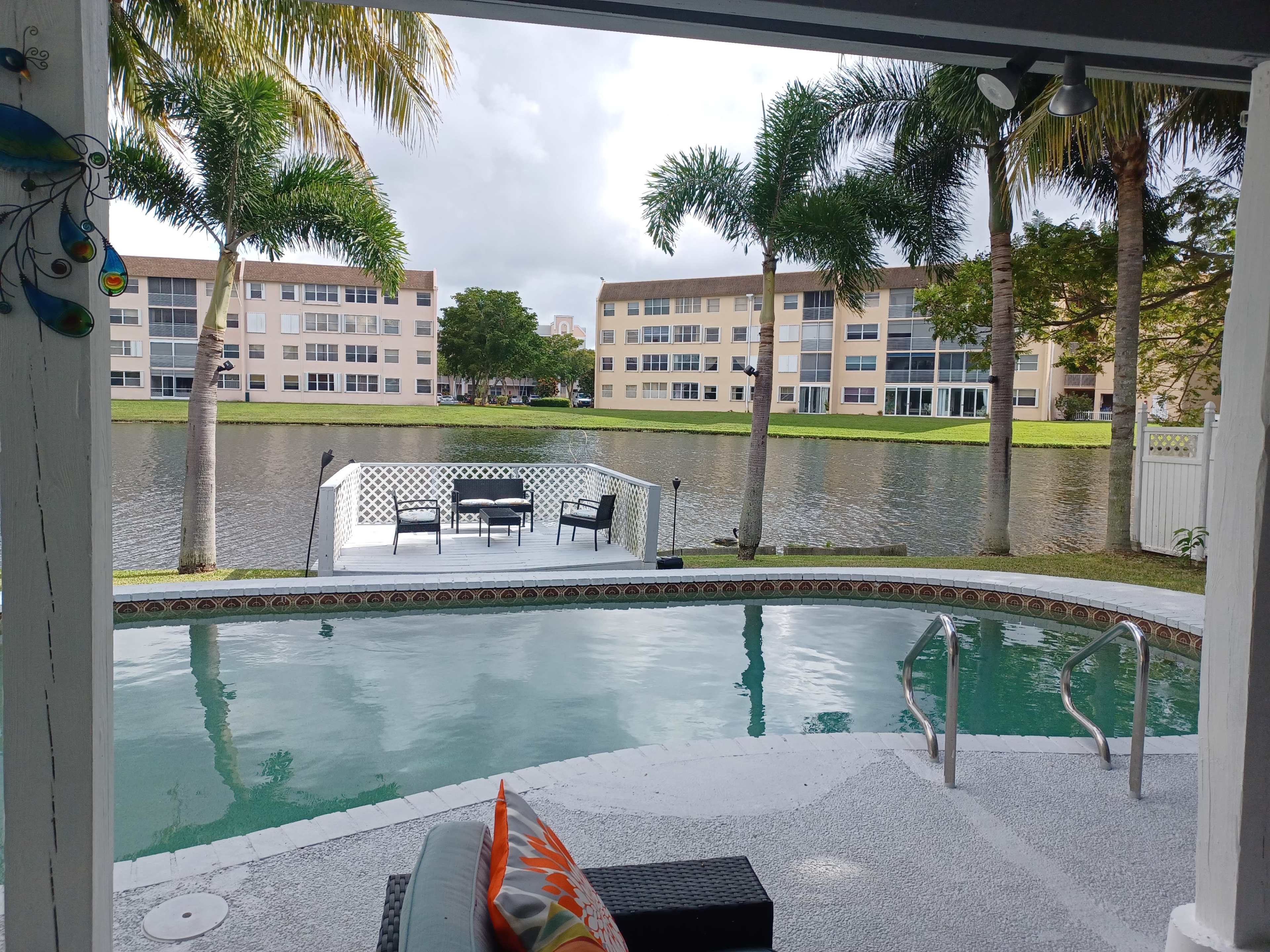 A pool area with a view of a calm lake and several apartment buildings in the background.