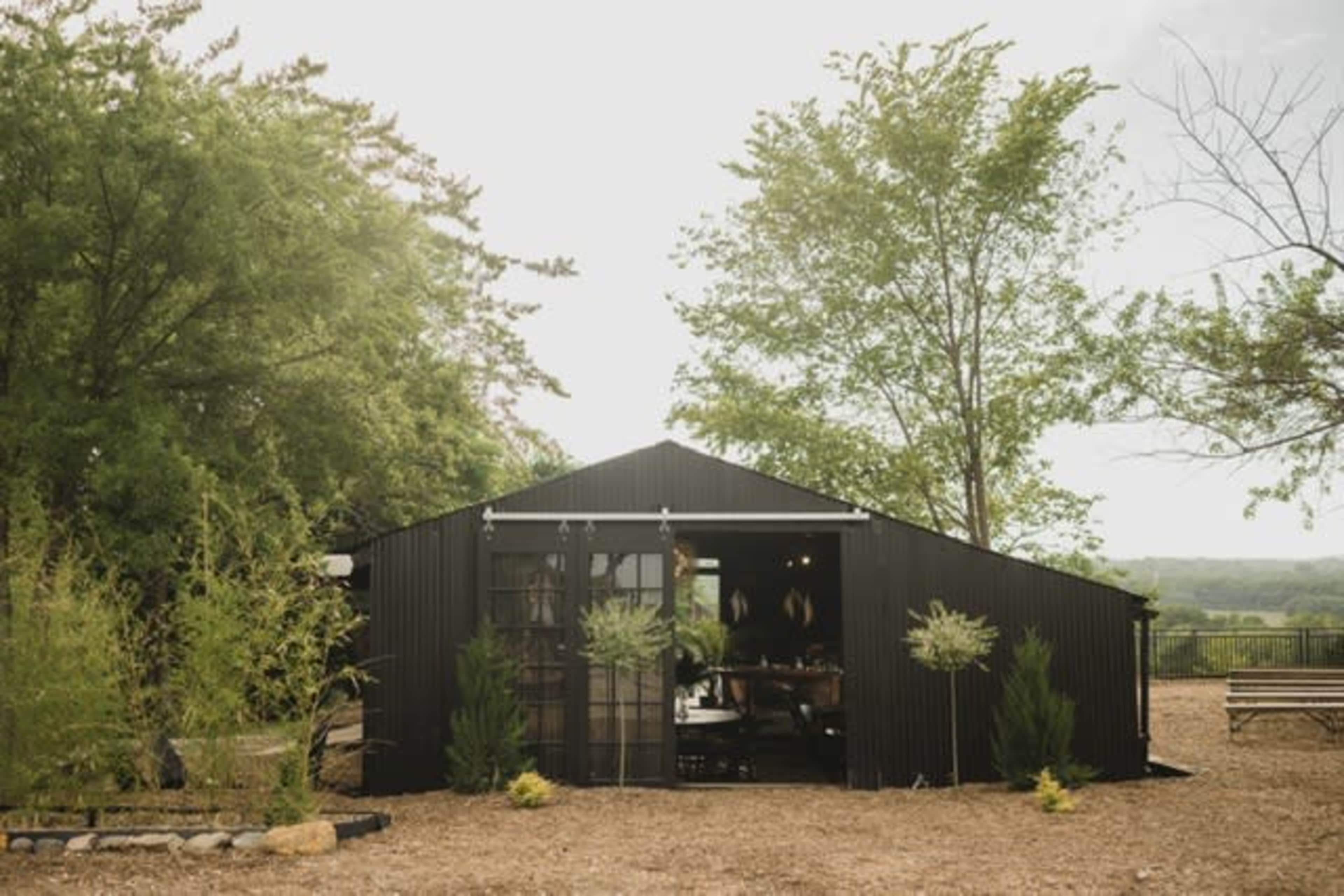 A black metal building sits among trees and landscaping in a rural setting.