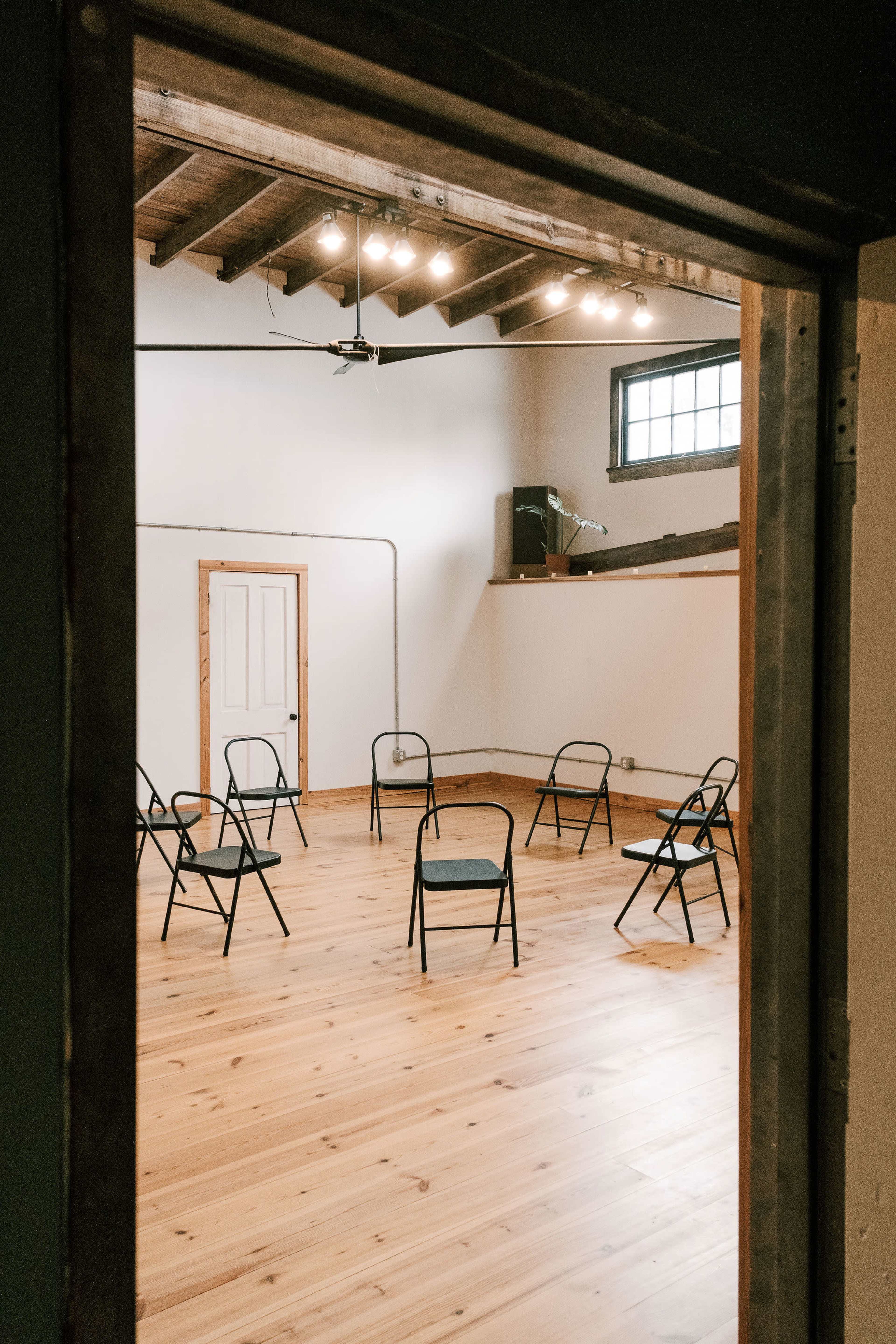 The image shows a room with wooden flooring and a circle of black folding chairs arranged in the center.