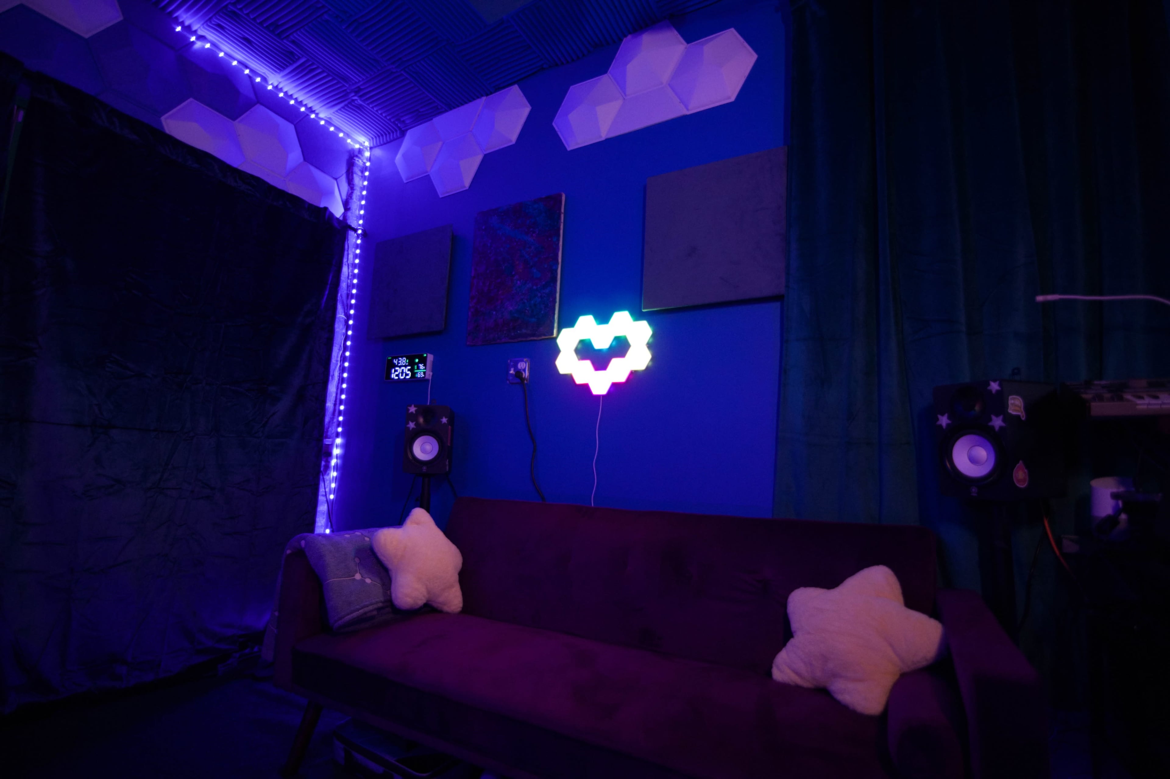 The image shows a cozy room with a purple couch, star-shaped pillows, colorful lighting, and sound equipment on one side.
