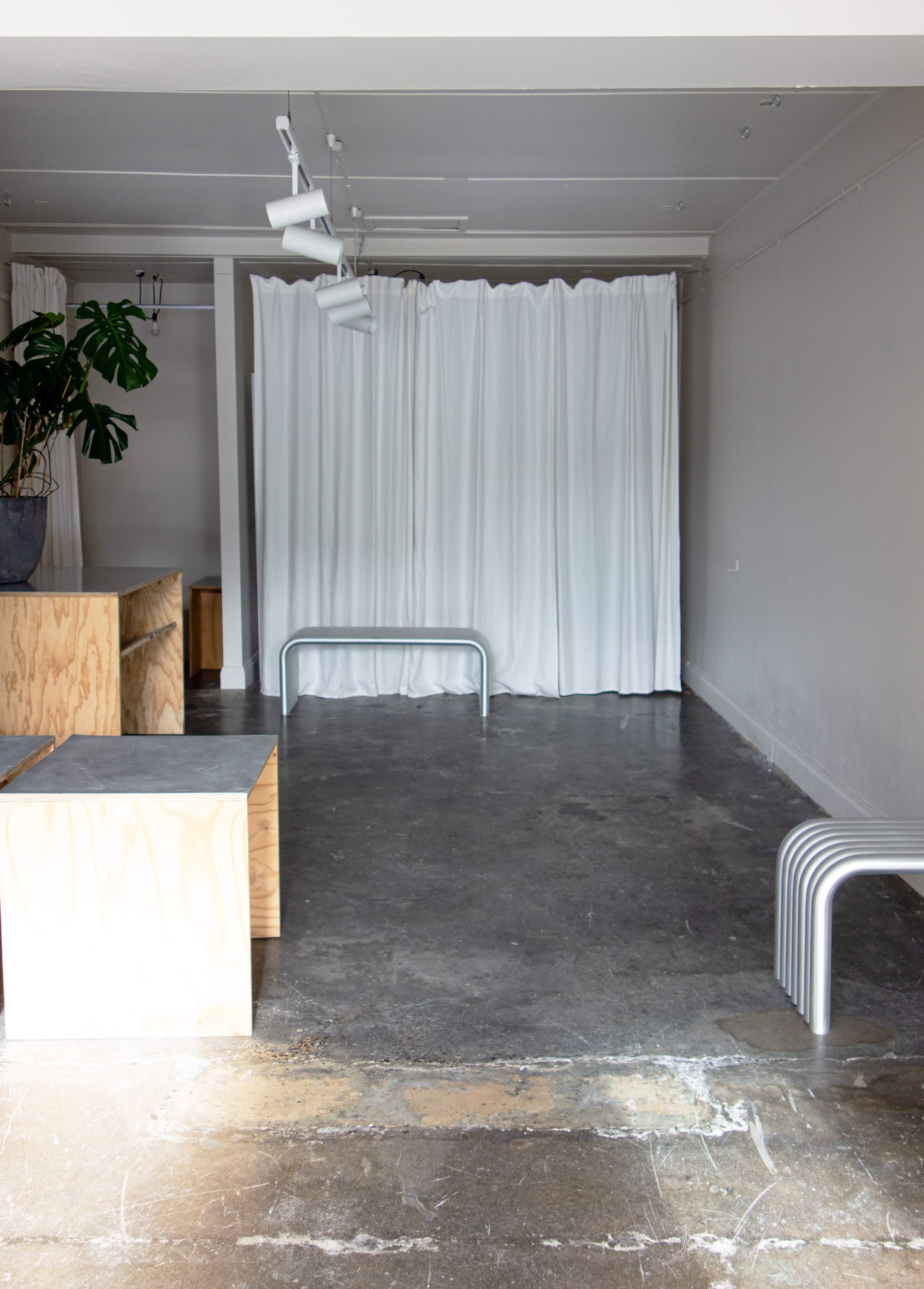 A minimalist interior space featuring a concrete floor, wooden furniture, a large plant, and a curtain partition.
