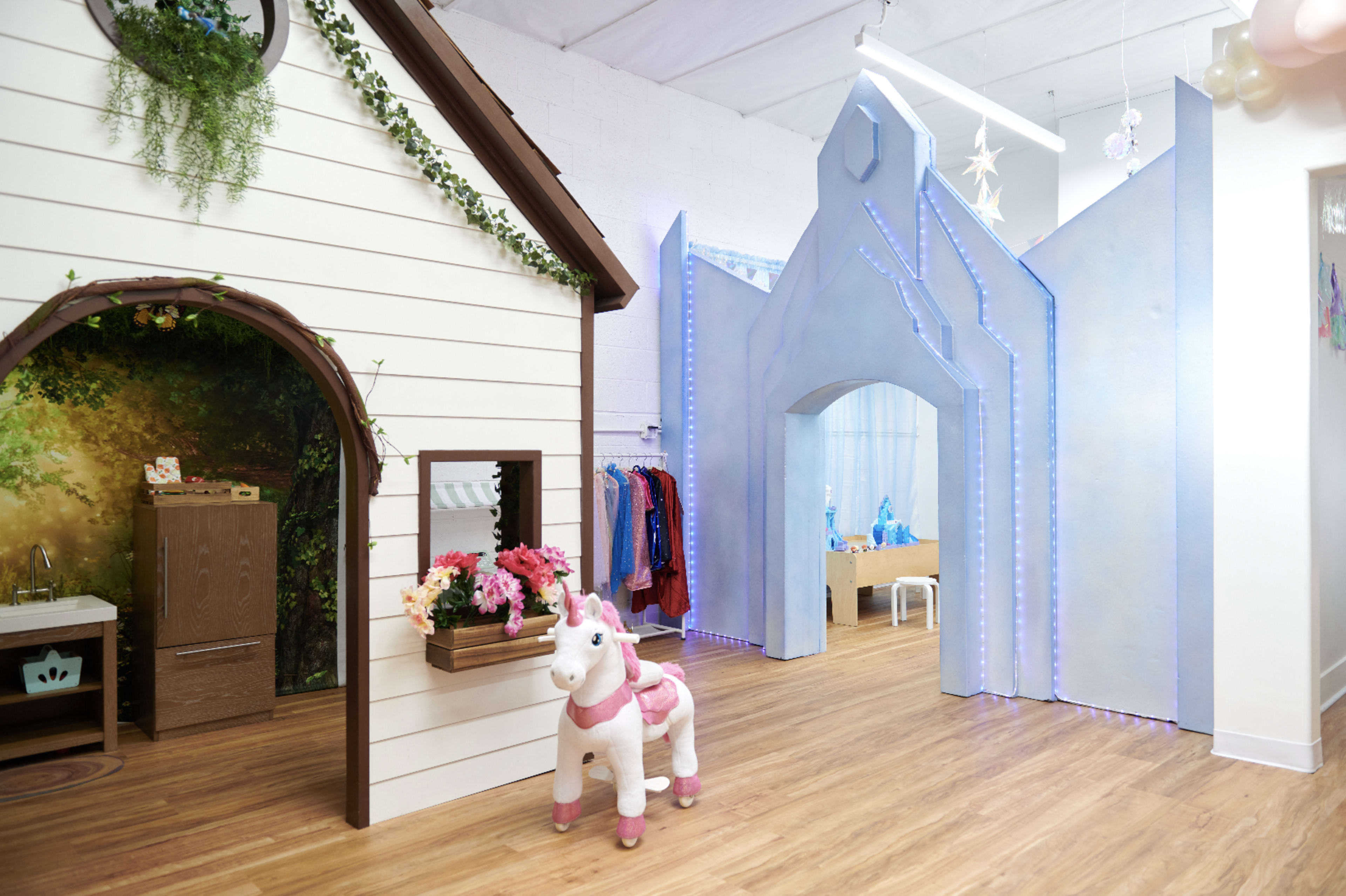 The image shows an indoor play area featuring a whimsical playhouse, a unicorn toy, and blue decorative arches.