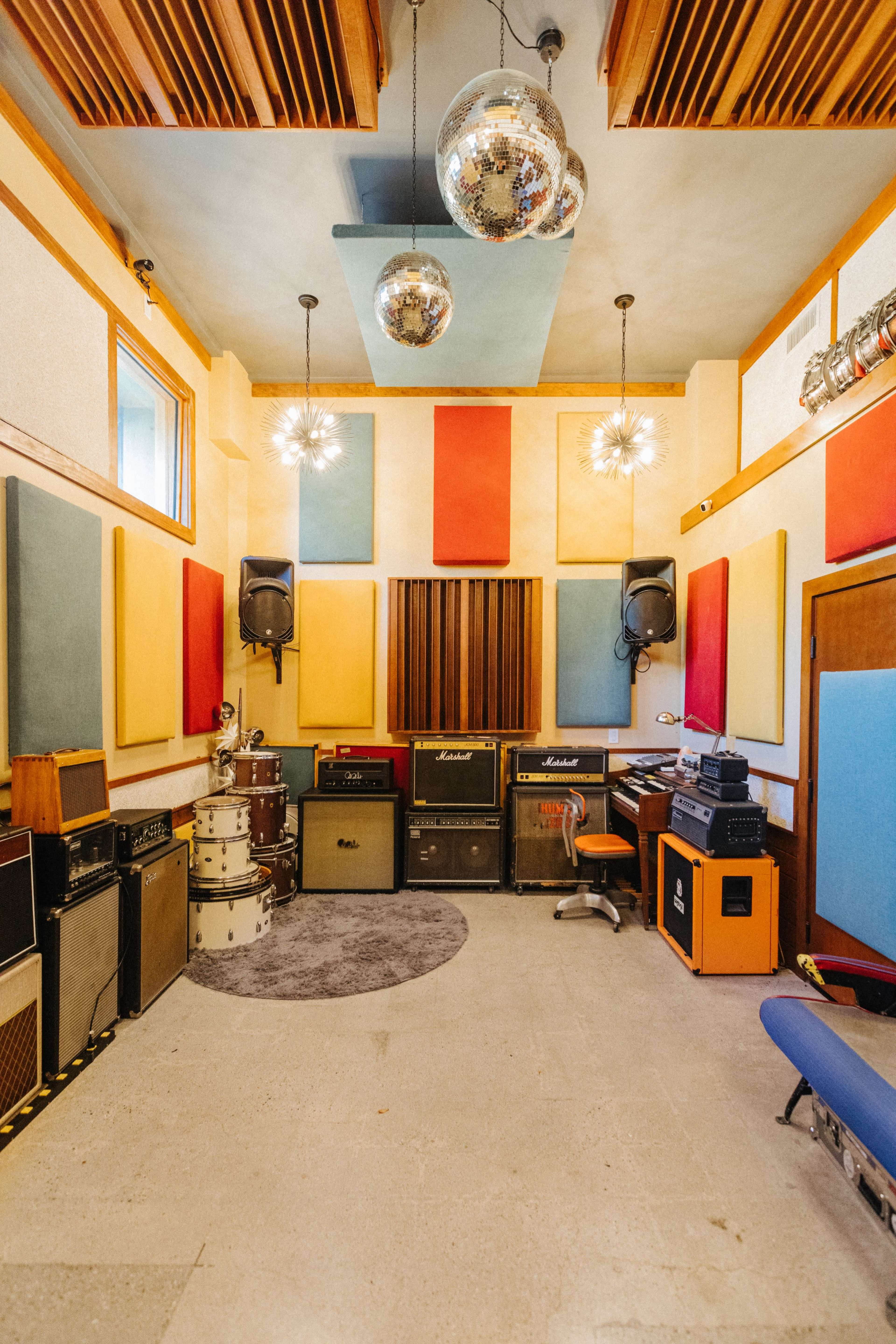 A music studio featuring colorful sound panels, various amplifiers, drums, and retro decor, with disco balls hanging from the ceiling.