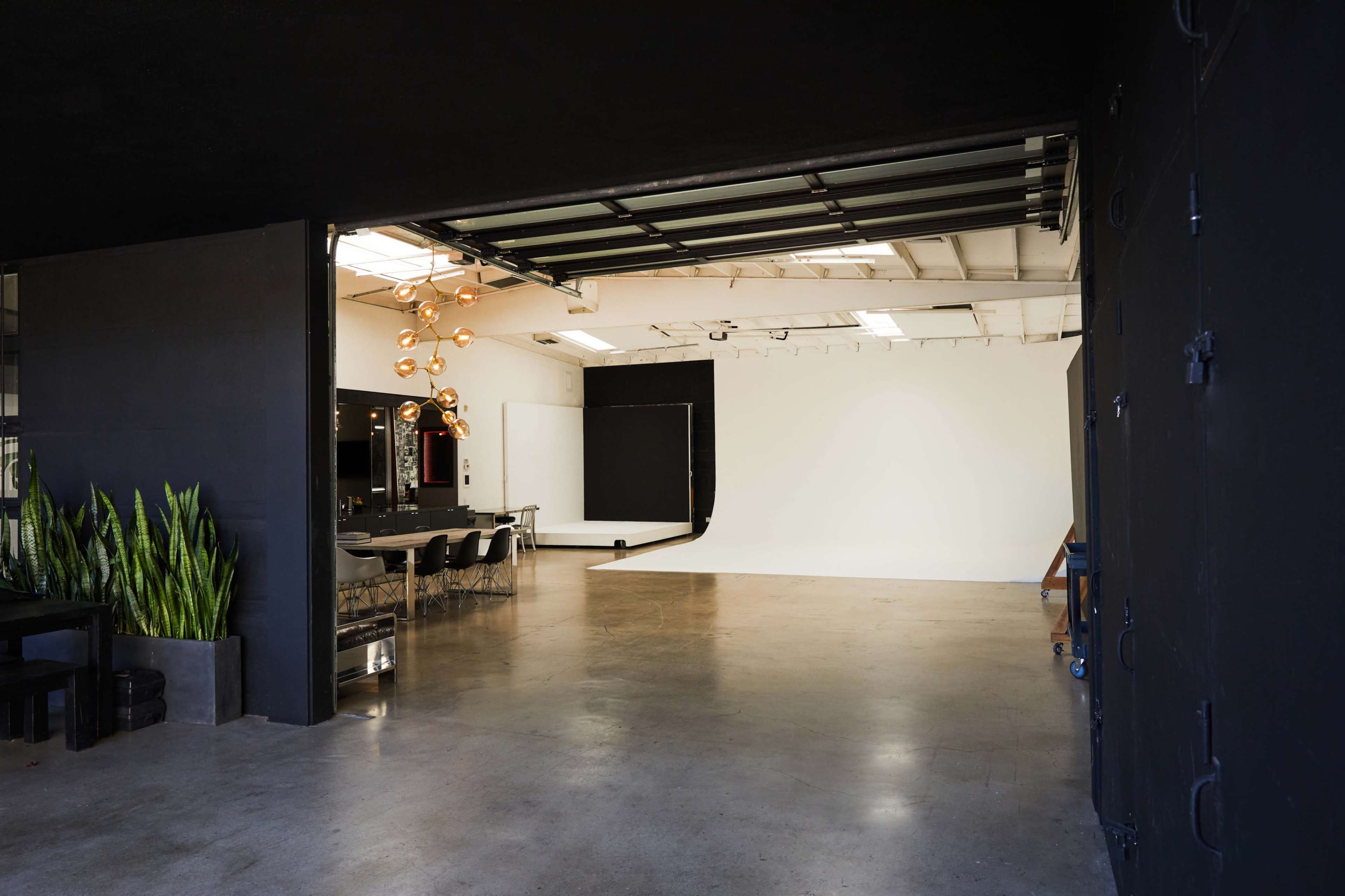 A contemporary studio space featuring a large white backdrop, a conference table with chairs, and modern lighting fixtures.