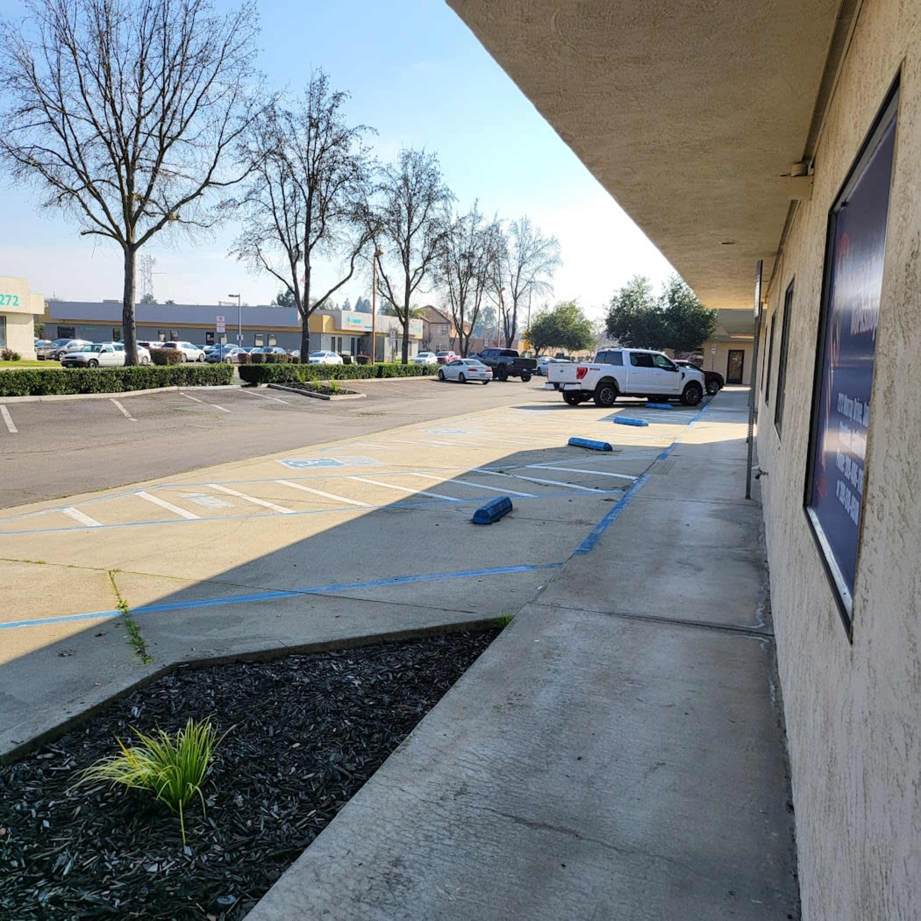 A parking lot with several vehicles, bordered by a building and lined with trees in the background.