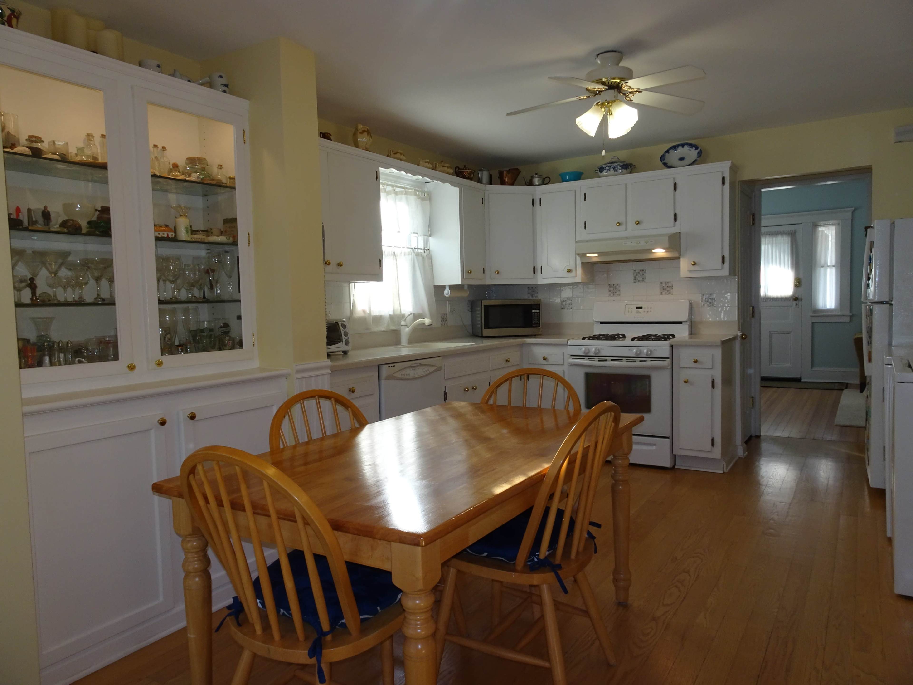 A bright kitchen with white cabinetry, a wooden dining table, and a window allowing natural light to enter.