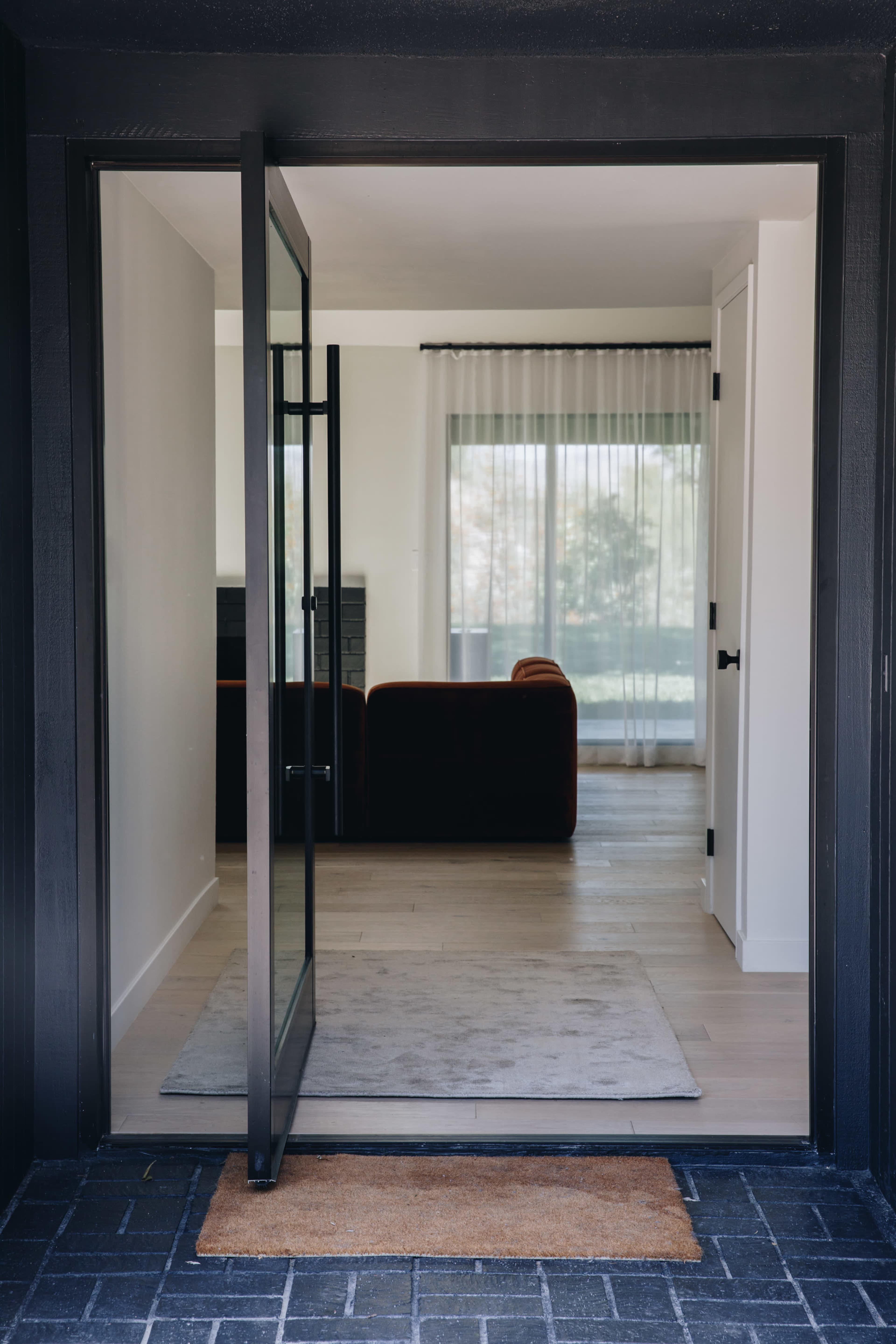 A doorway leading into a living room with a couch and large windows covered by sheer curtains.