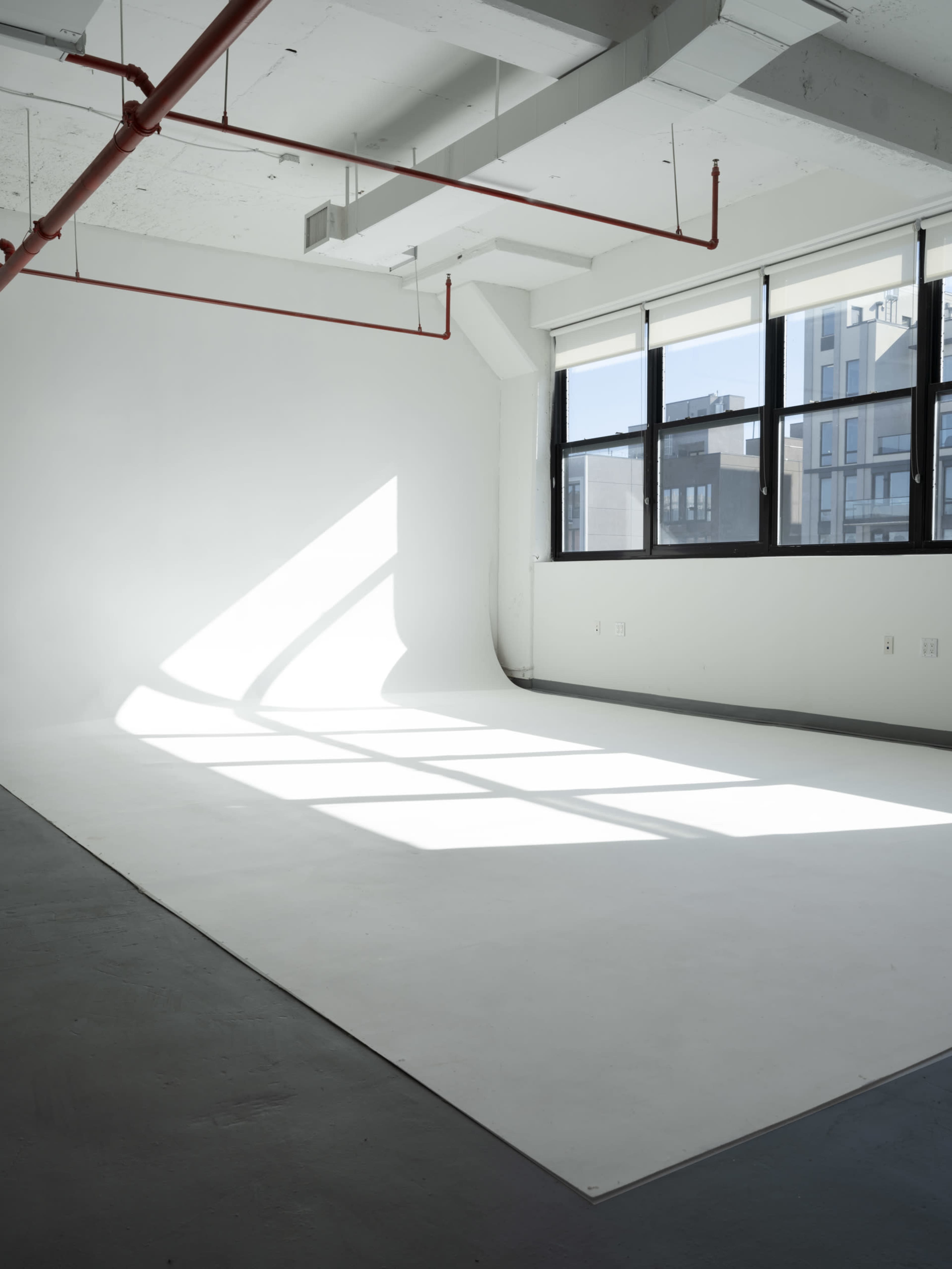 A bright, empty studio space with a white backdrop and large windows casting shadows on the floor.