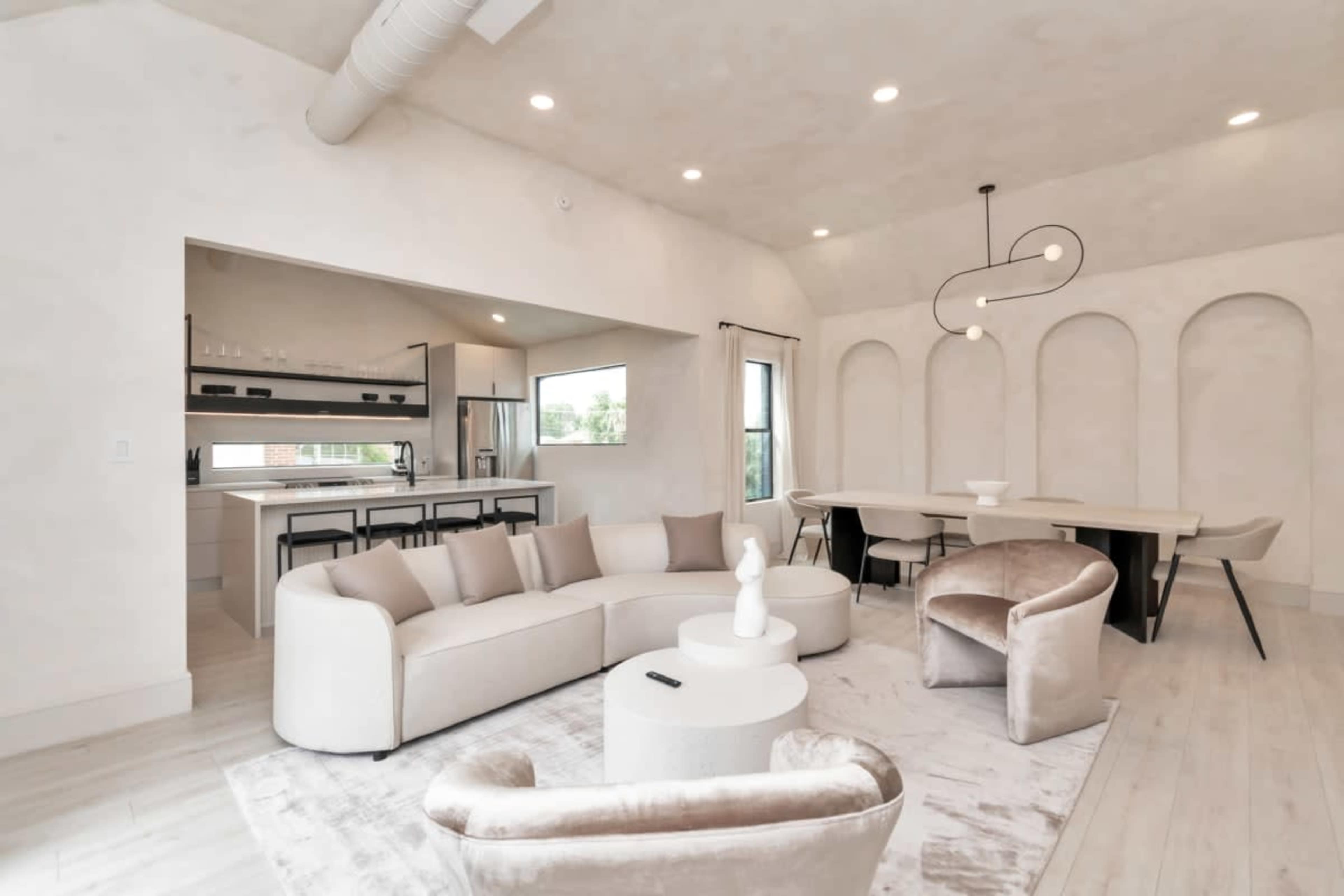 A modern living space featuring a curved sectional sofa, arched wall recesses, a dining area, and a minimalist kitchen.