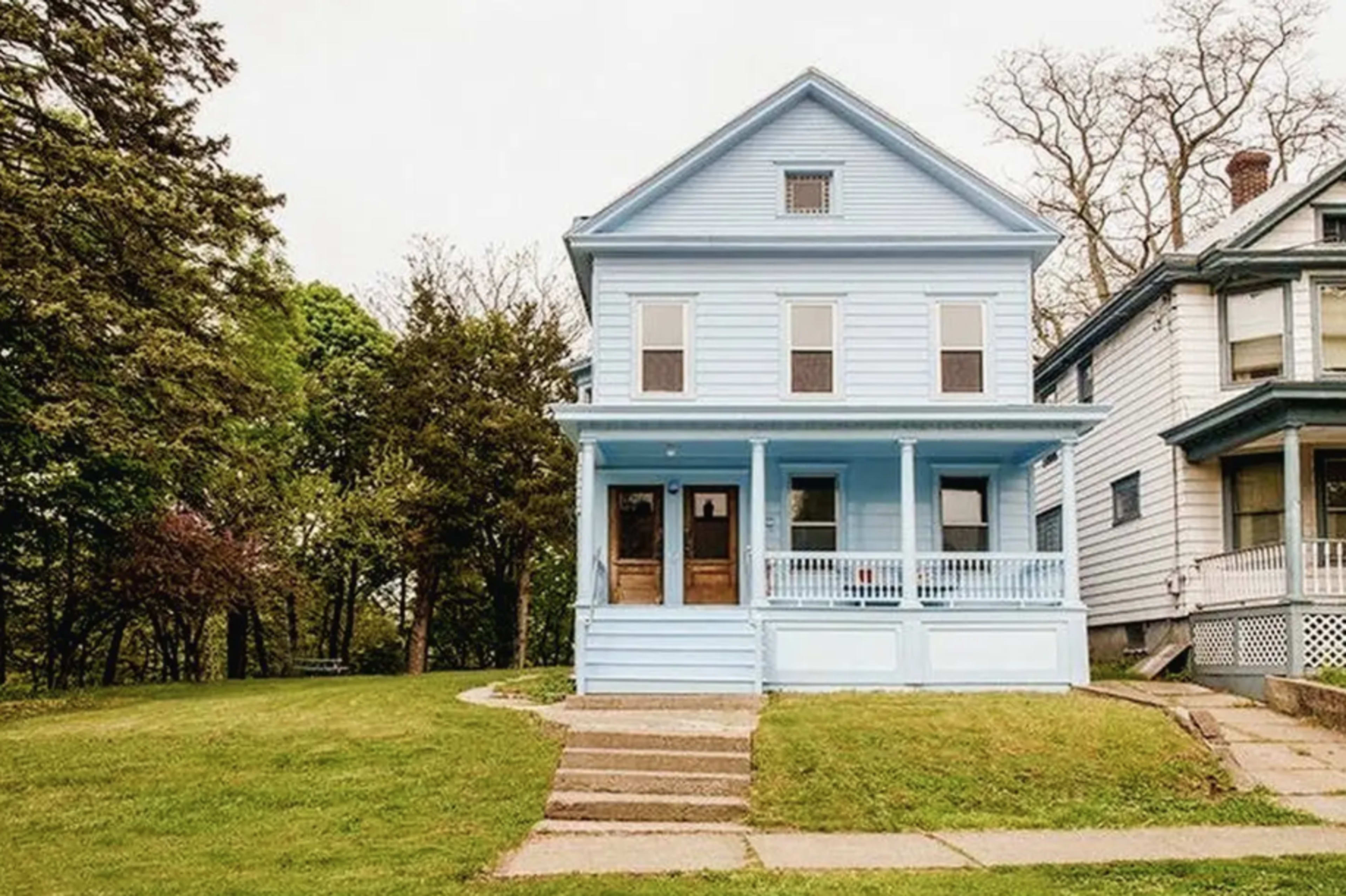 A blue two-story house with a front porch and a grassy yard, situated next to another similar house.