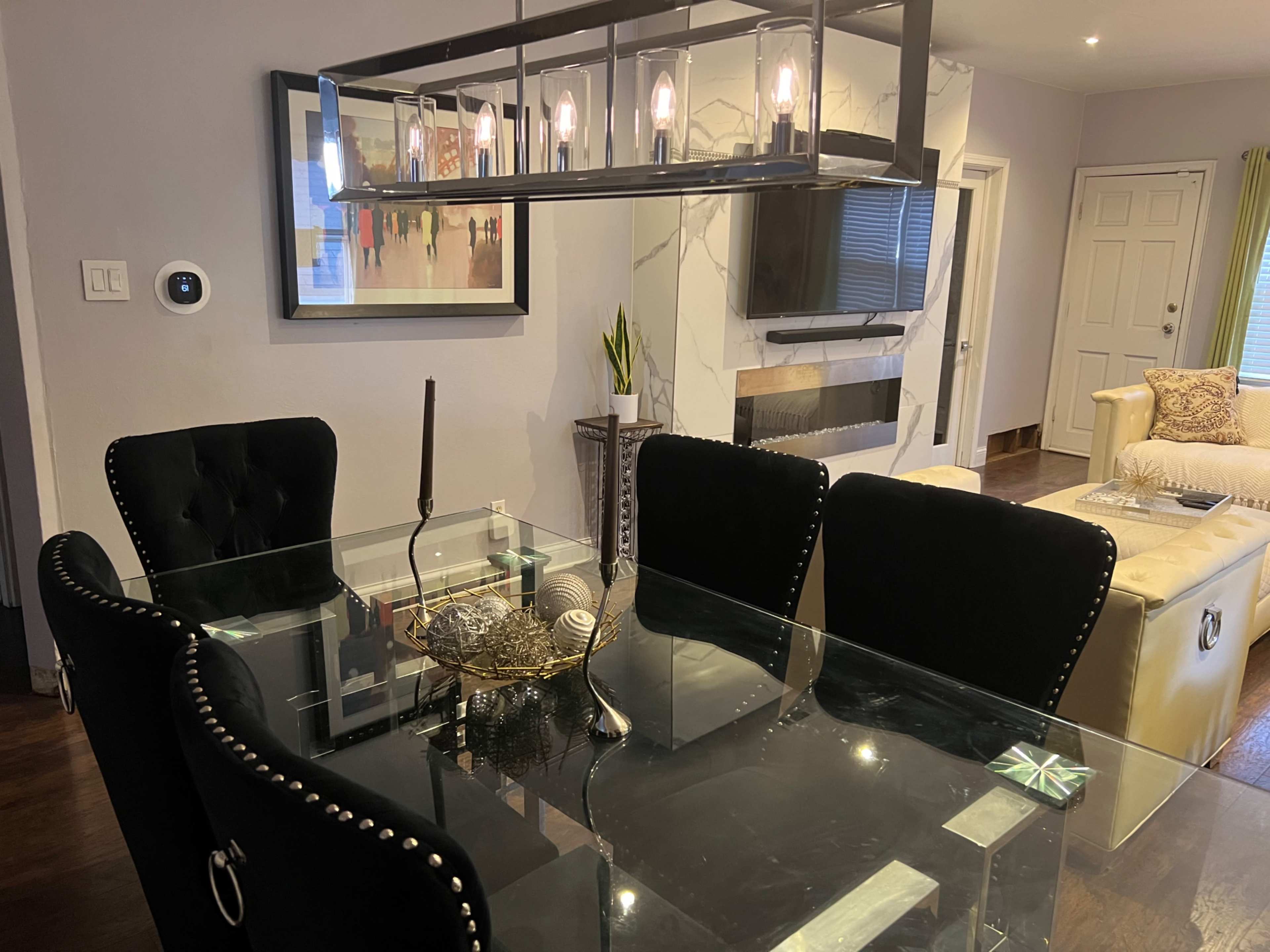 A modern dining area featuring a glass table with black chairs, a ceiling light fixture, and a wall-mounted television.