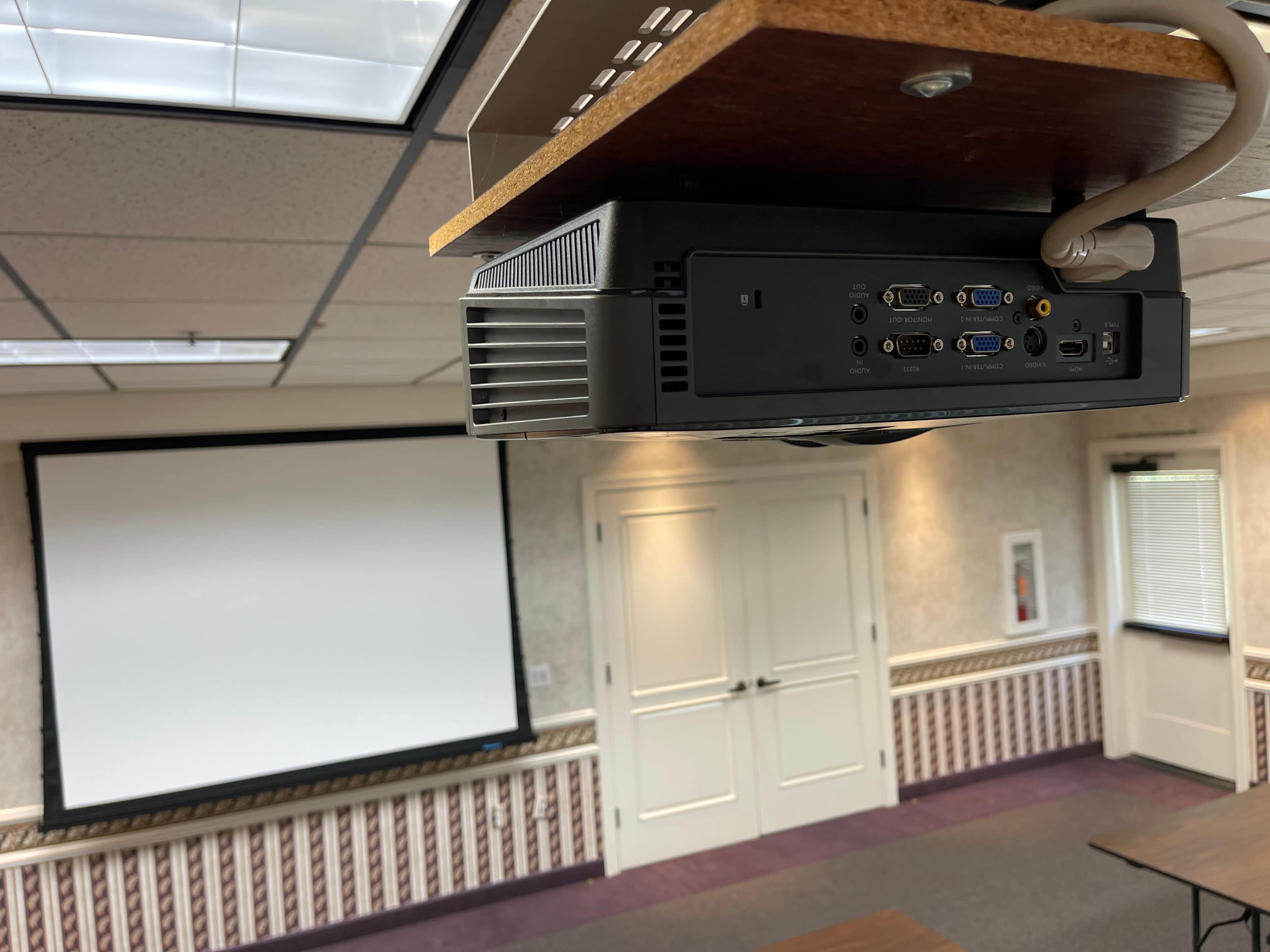 A ceiling-mounted projector facing a large blank projection screen in a conference room.