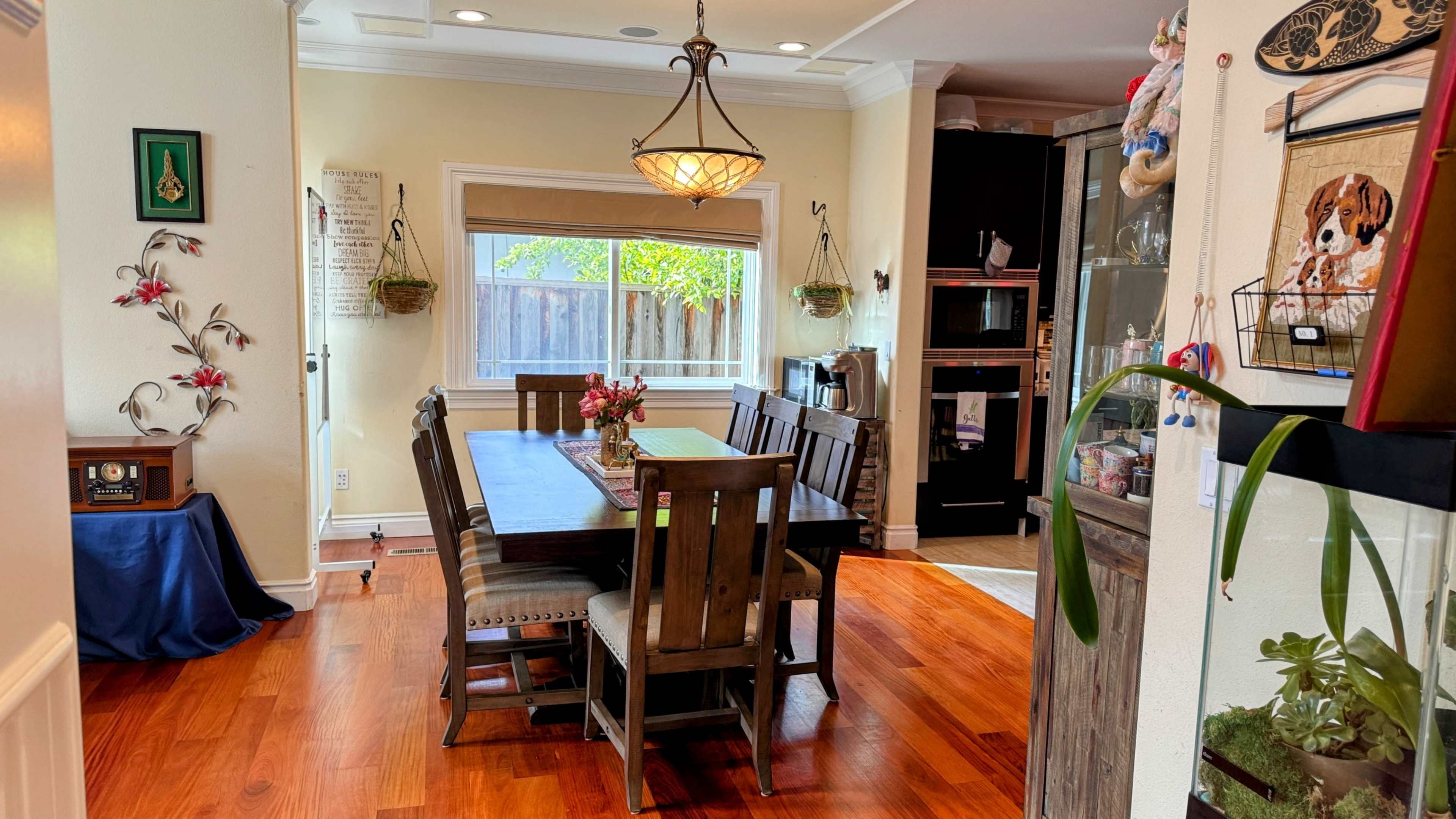A dining area features a wooden table surrounded by matching chairs, with a large window providing natural light and a view of the outdoors.