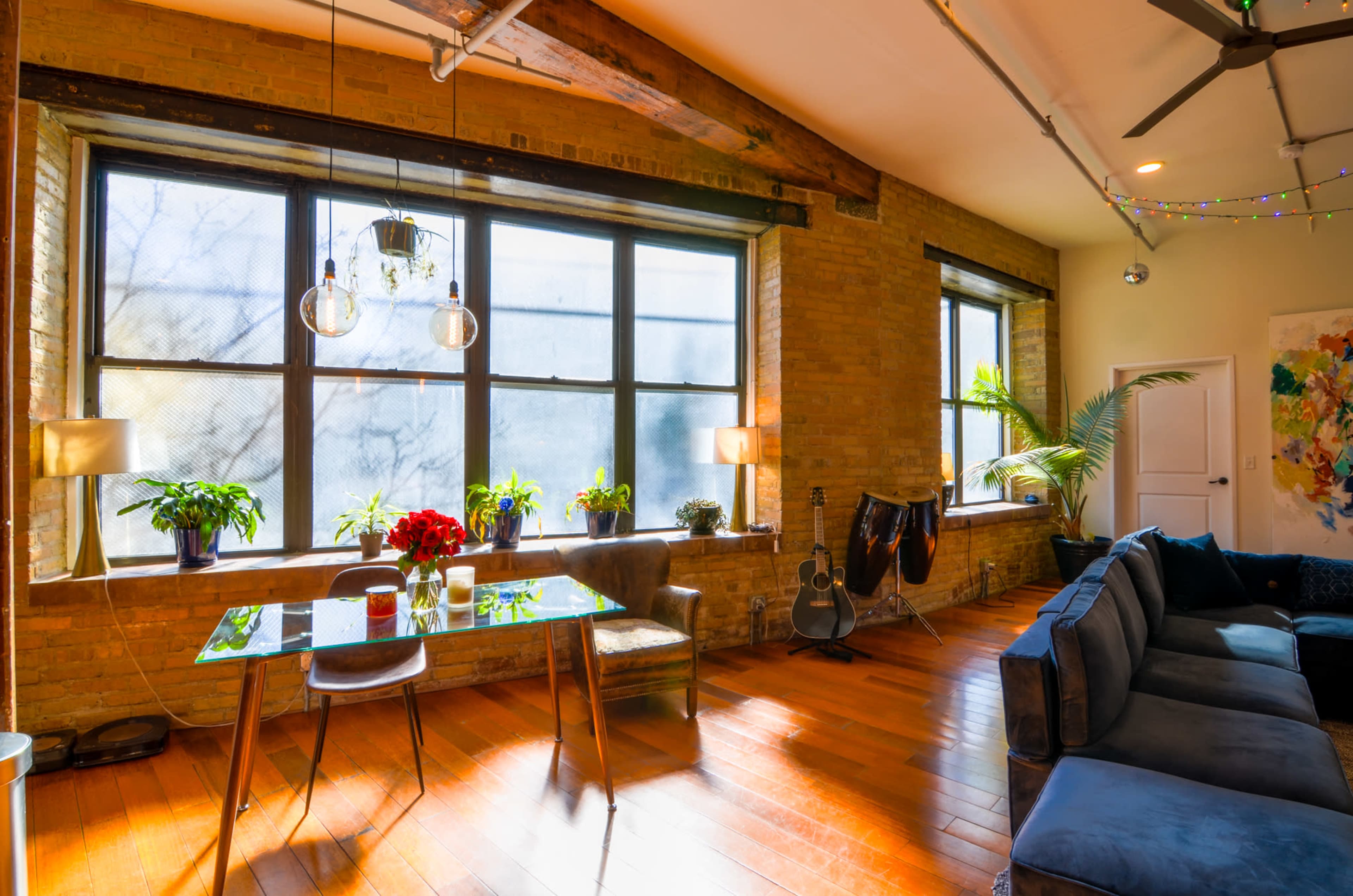 A bright, modern living space with large windows, wooden floors, and a dining table surrounded by plants.