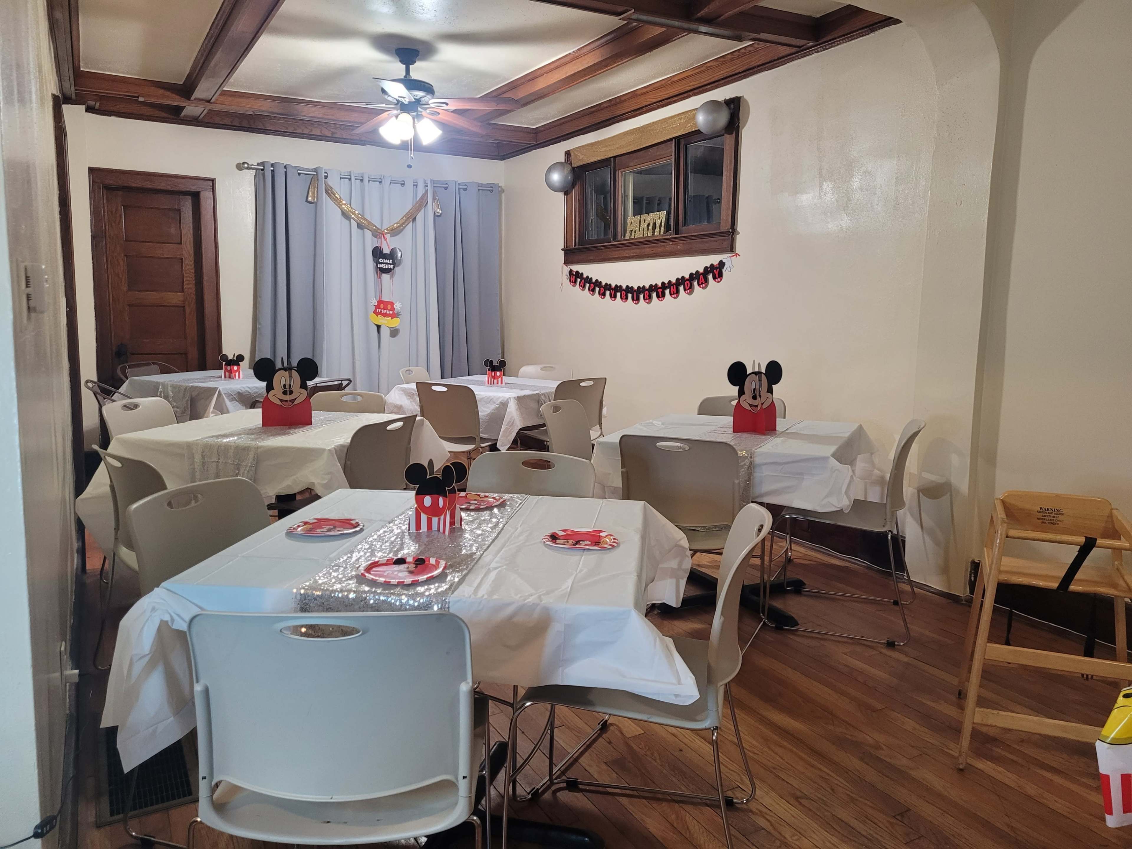 A decorated dining room with multiple tables covered in white tablecloths and adorned with Mickey Mouse-themed centerpieces.