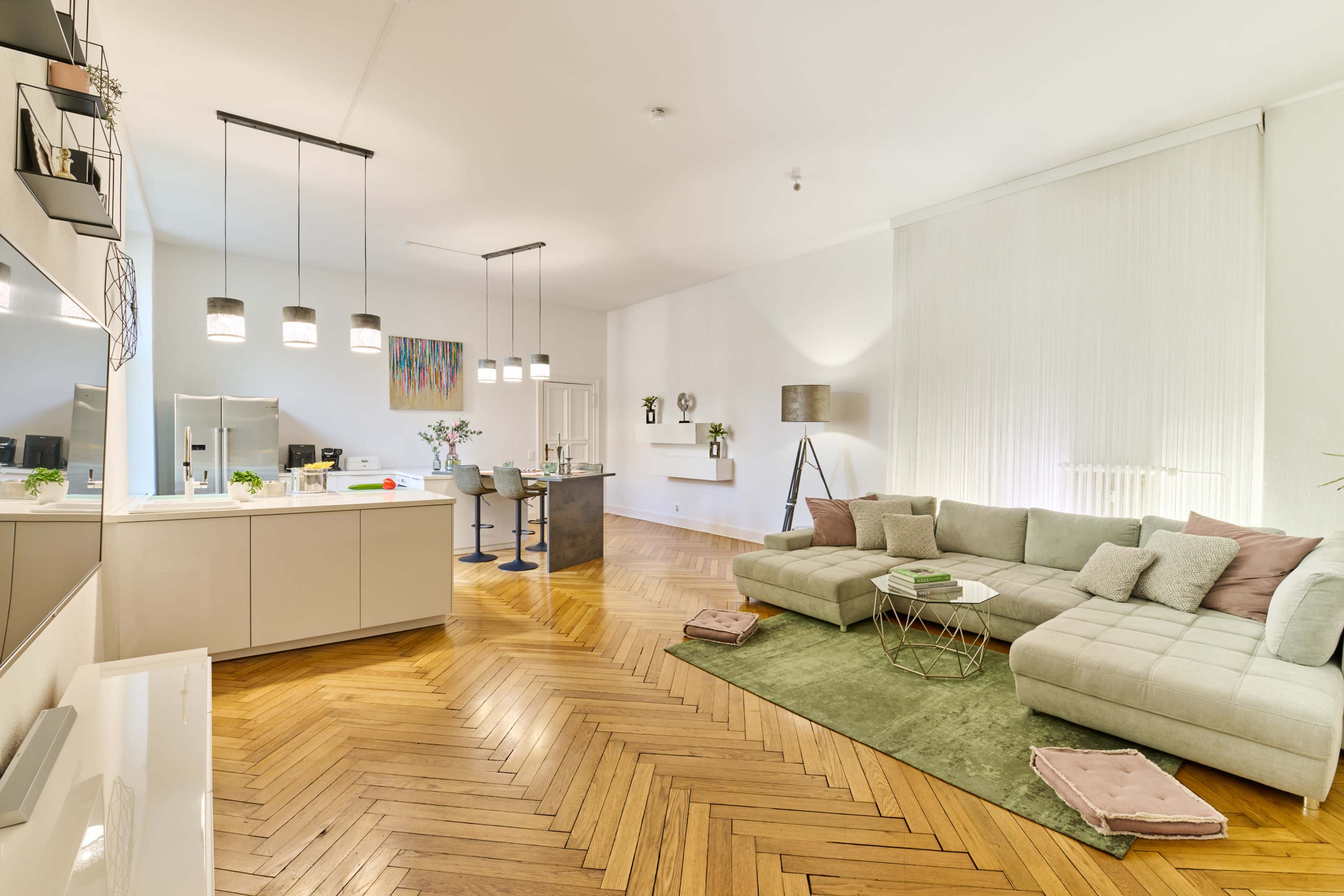 A modern living space featuring a sectional sofa, a green area rug, and a kitchen island with pendant lighting.