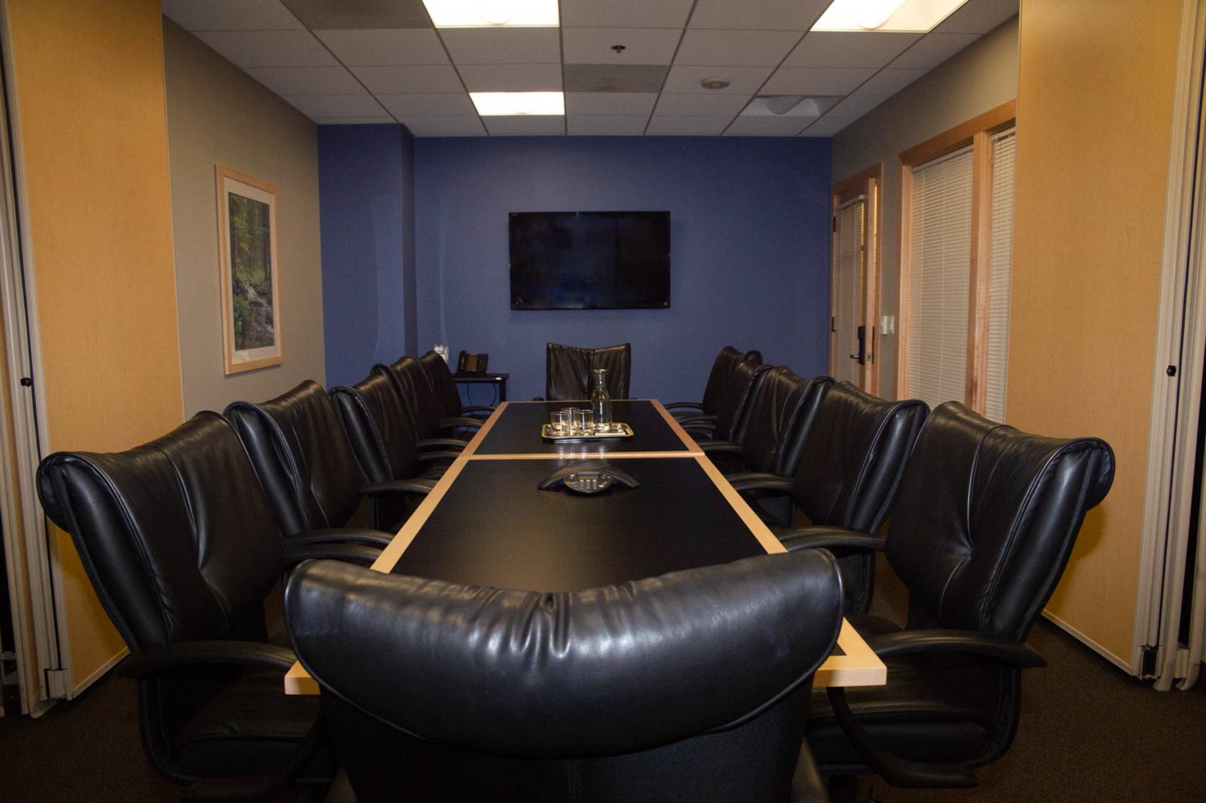A conference room with a long, rectangular table surrounded by black leather chairs, and a wall-mounted television at one end.