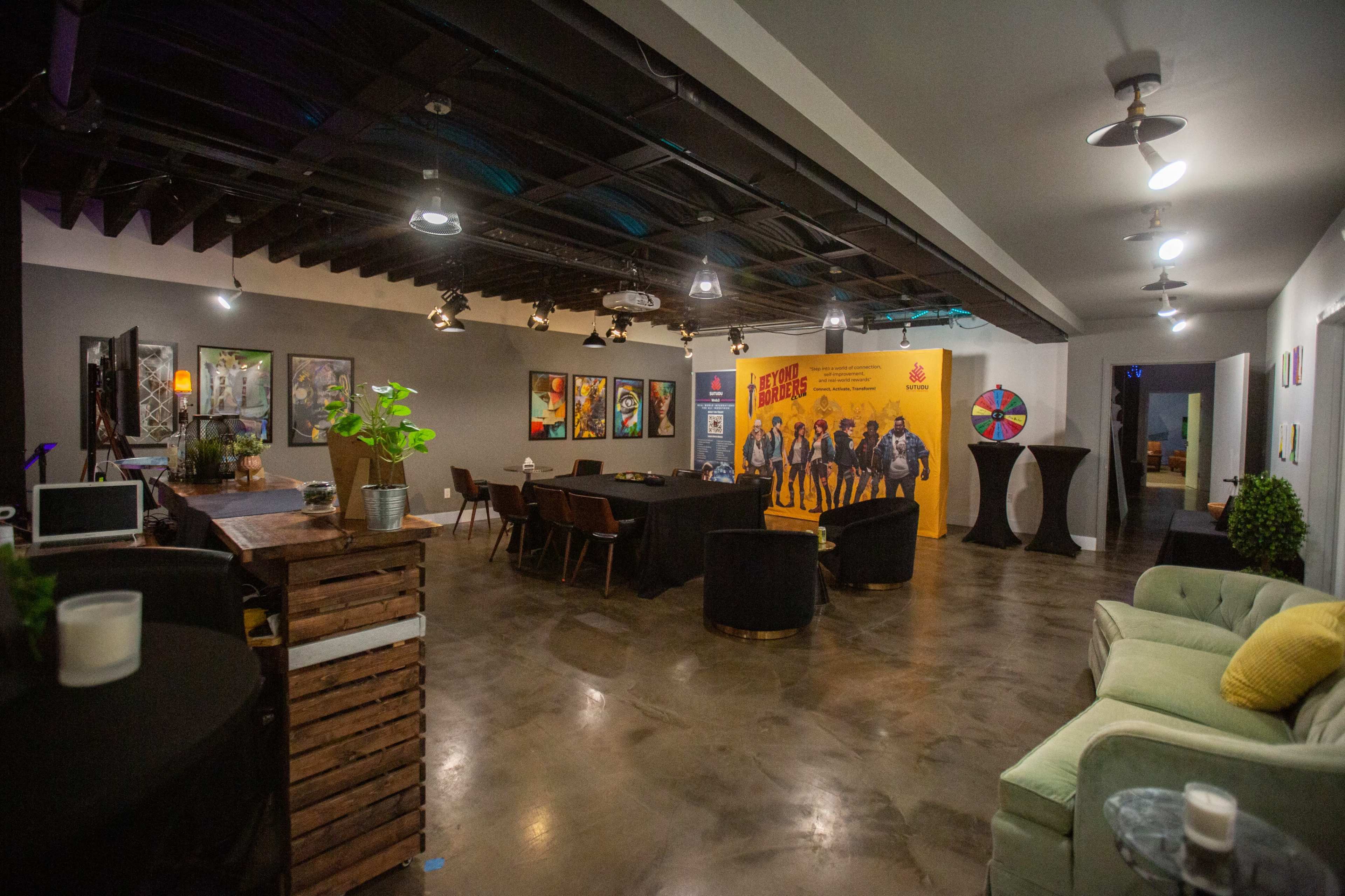 A spacious event room with various seating arrangements, artwork on the walls, and a backdrop featuring a promotional display.