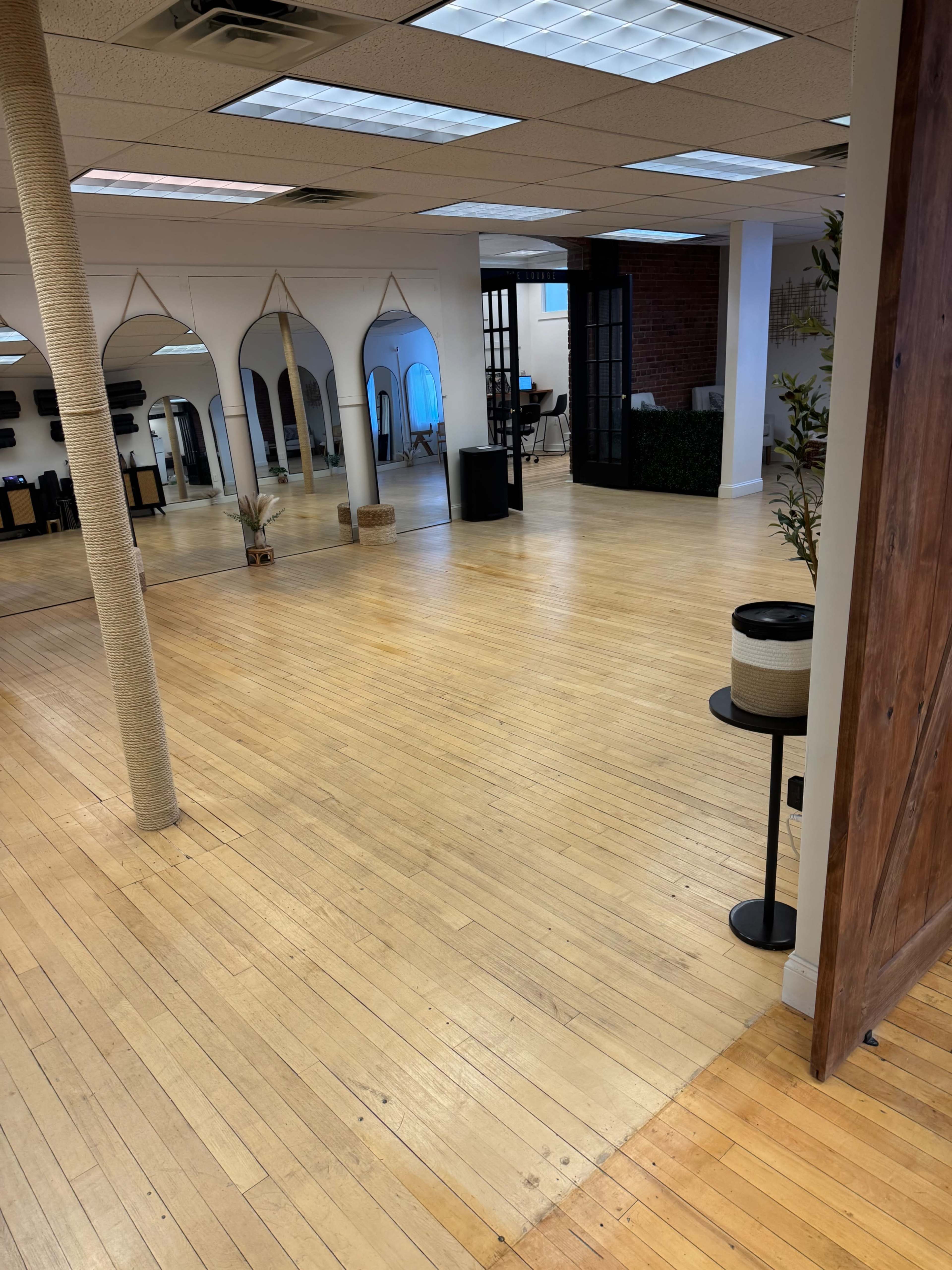 The image shows a spacious, empty room with wooden floors, arched mirrors, and a black-framed room divider in the background.