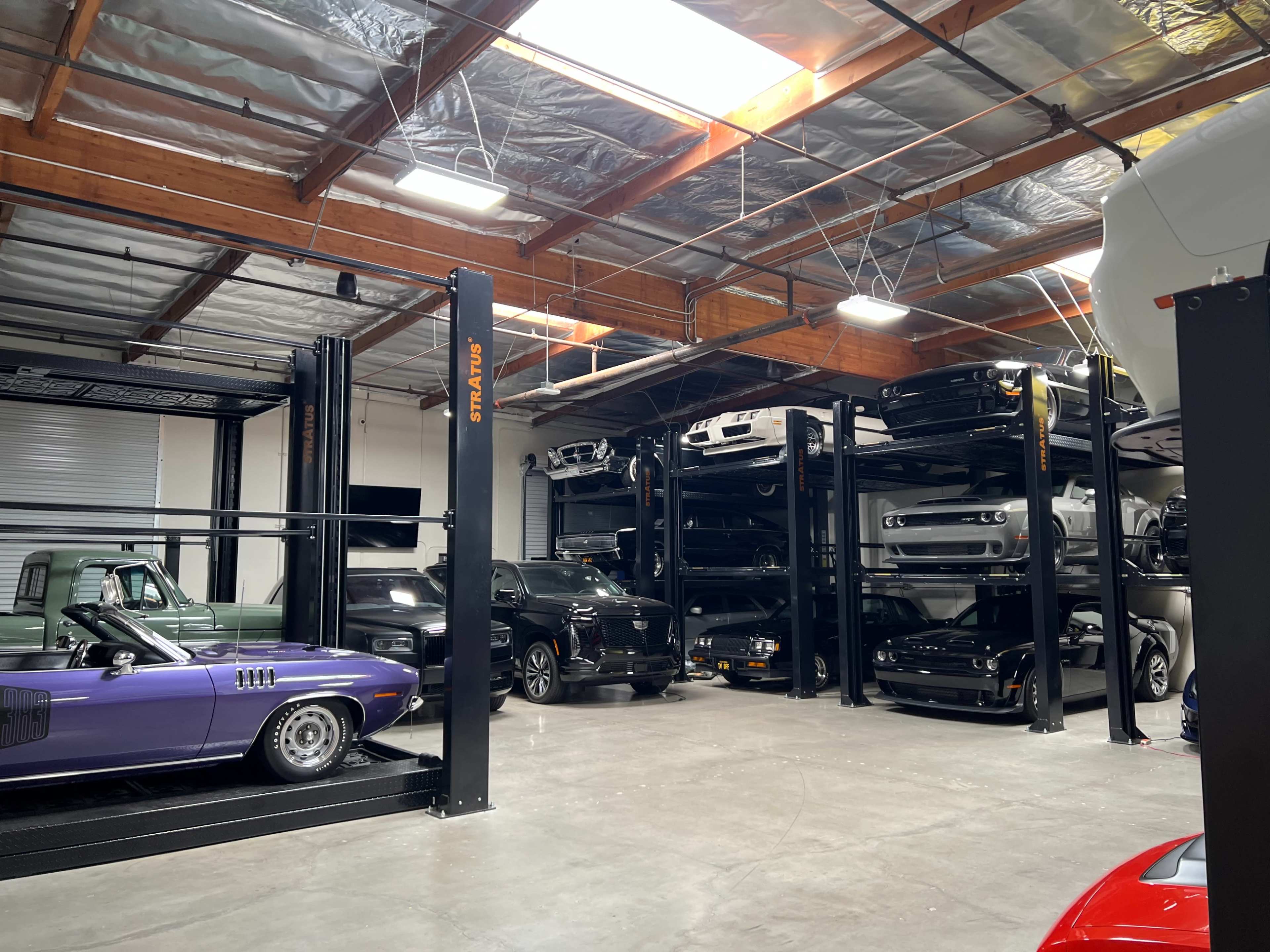 The image shows a spacious automotive storage facility with multiple car lifts displaying various cars, including classic and modern vehicles.