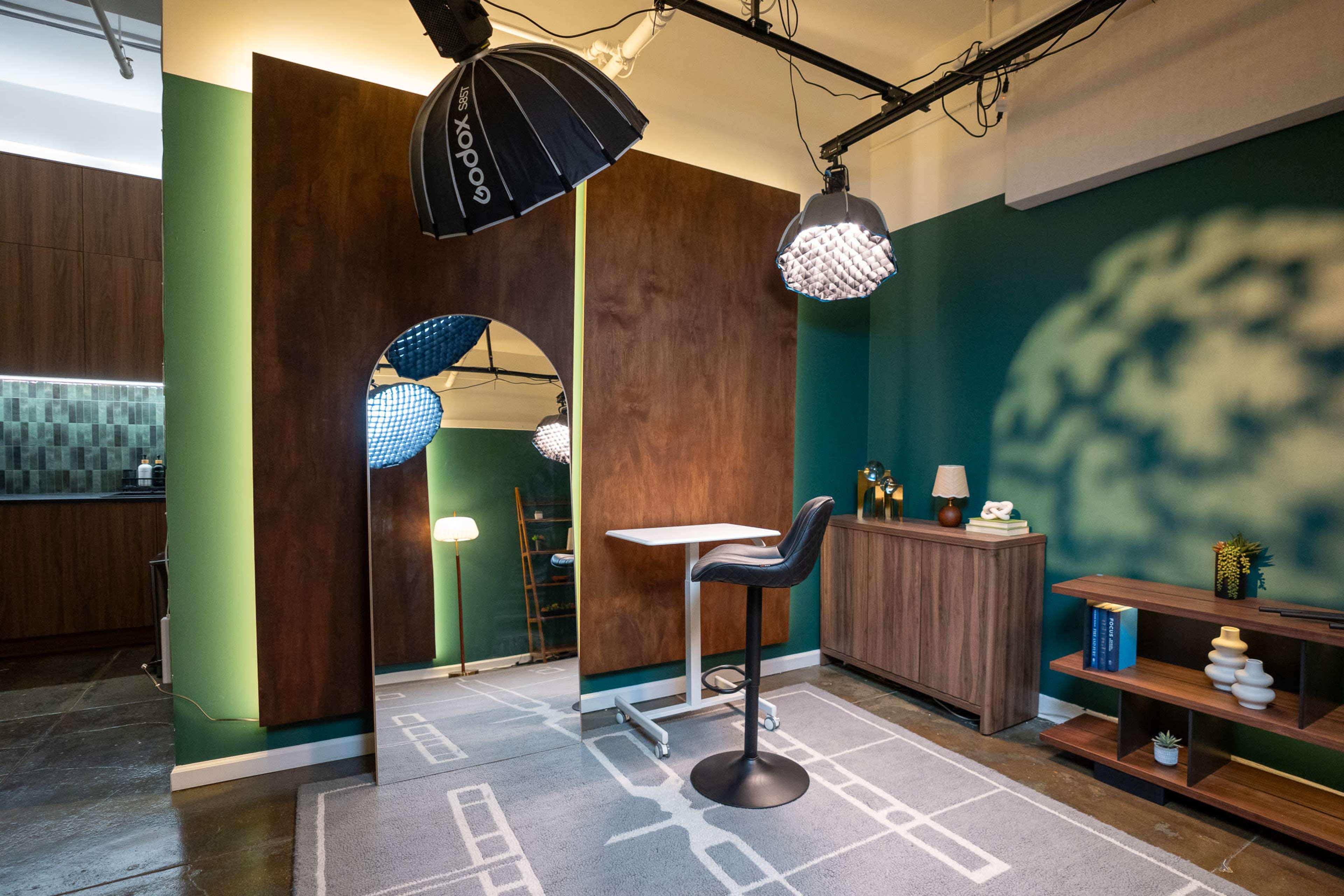 The image shows a modern interior space featuring a wooden accent wall, a bar stool next to a small table, and various decorative elements, including lamps and a bookshelf.