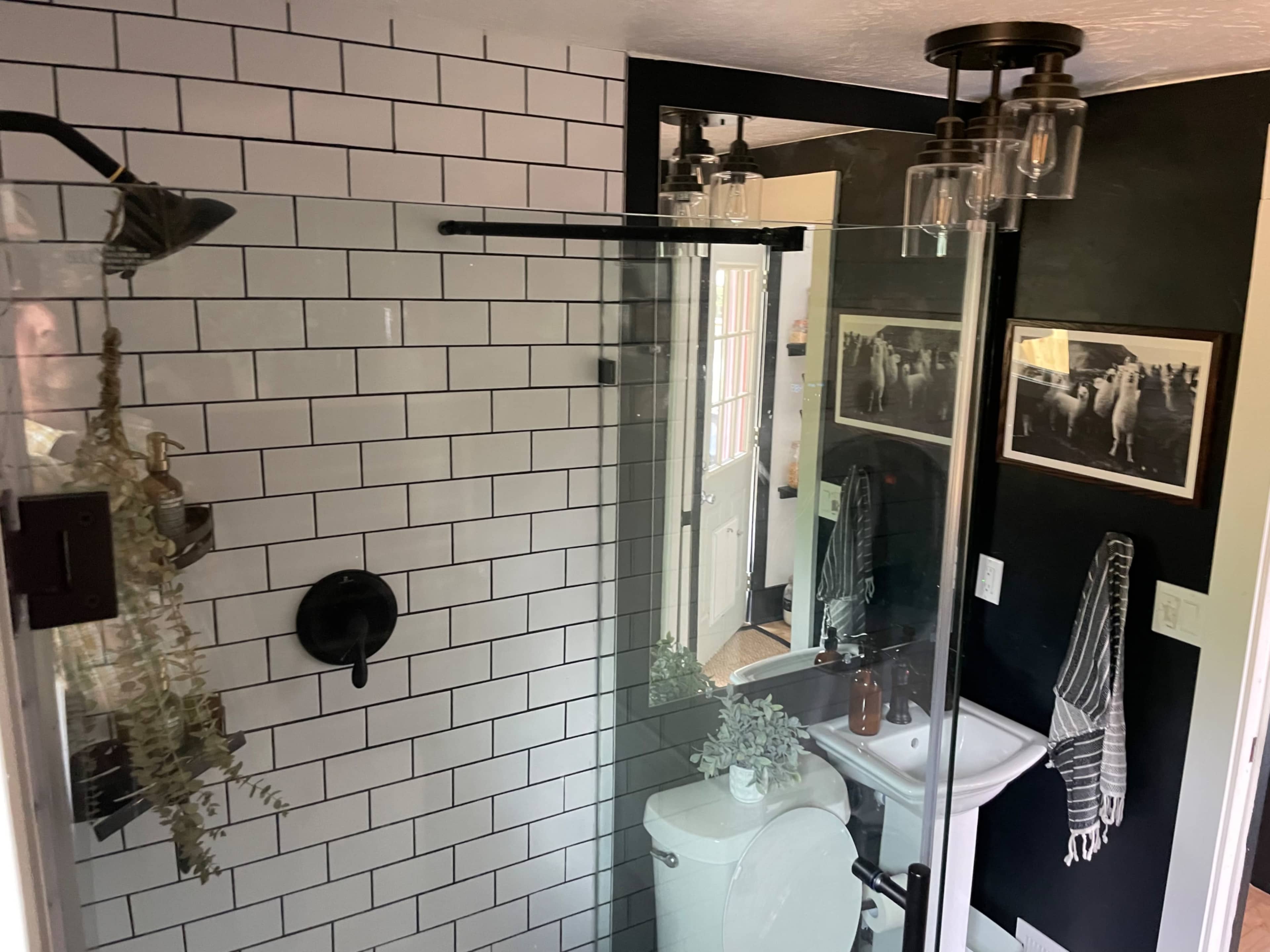A modern bathroom featuring a glass shower enclosure, white subway tile walls, and a vintage-style sink with a mirror.